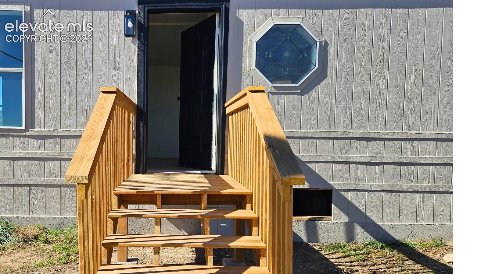 Exterior entrance featuring wood-finished steps and railings, a geometric accent window, and a contrasting entry door frame