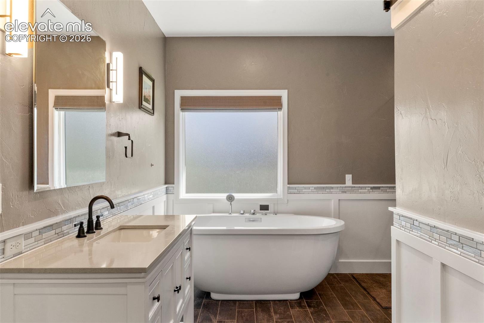 Bathroom with vanity, a freestanding bath, a textured wall, wood finish floors, and a wainscoted wall