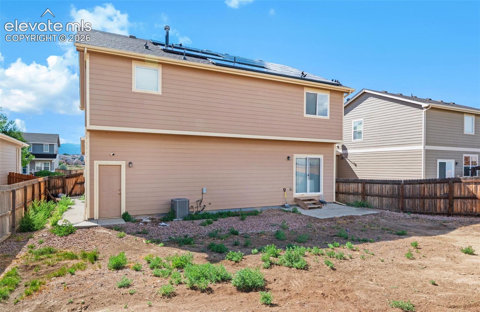 Two-story exterior featuring lap siding, roof-mounted solar panels, sliding glass patio doors, and a wood privacy fence
