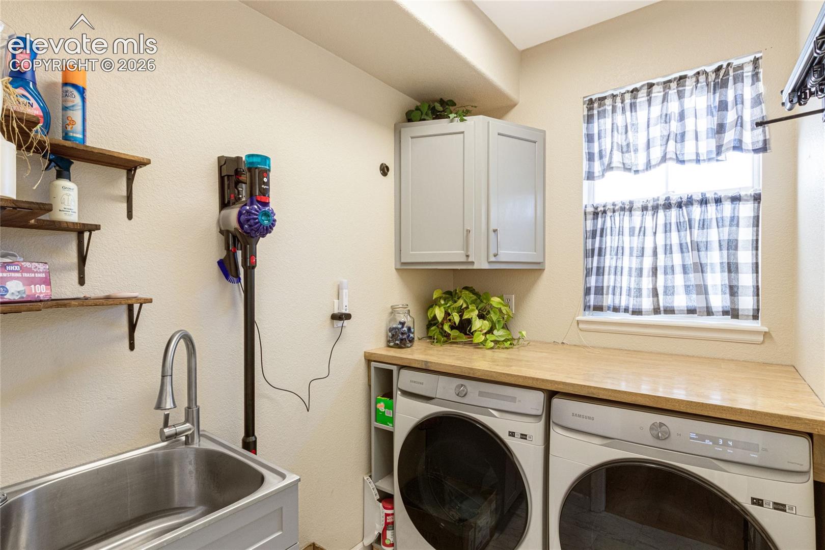 Utility area featuring a stainless steel drop-in sink with a high-arch faucet, butcher block countertop, grey upper cabinetry, and open wood shelving