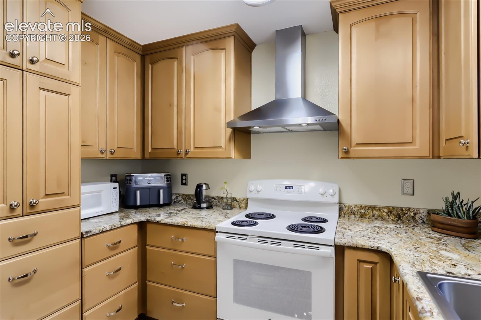 Kitchen featuring light wood cabinetry with brushed nickel hardware, granite-style countertops, a stainless steel range hood, and a white electric range