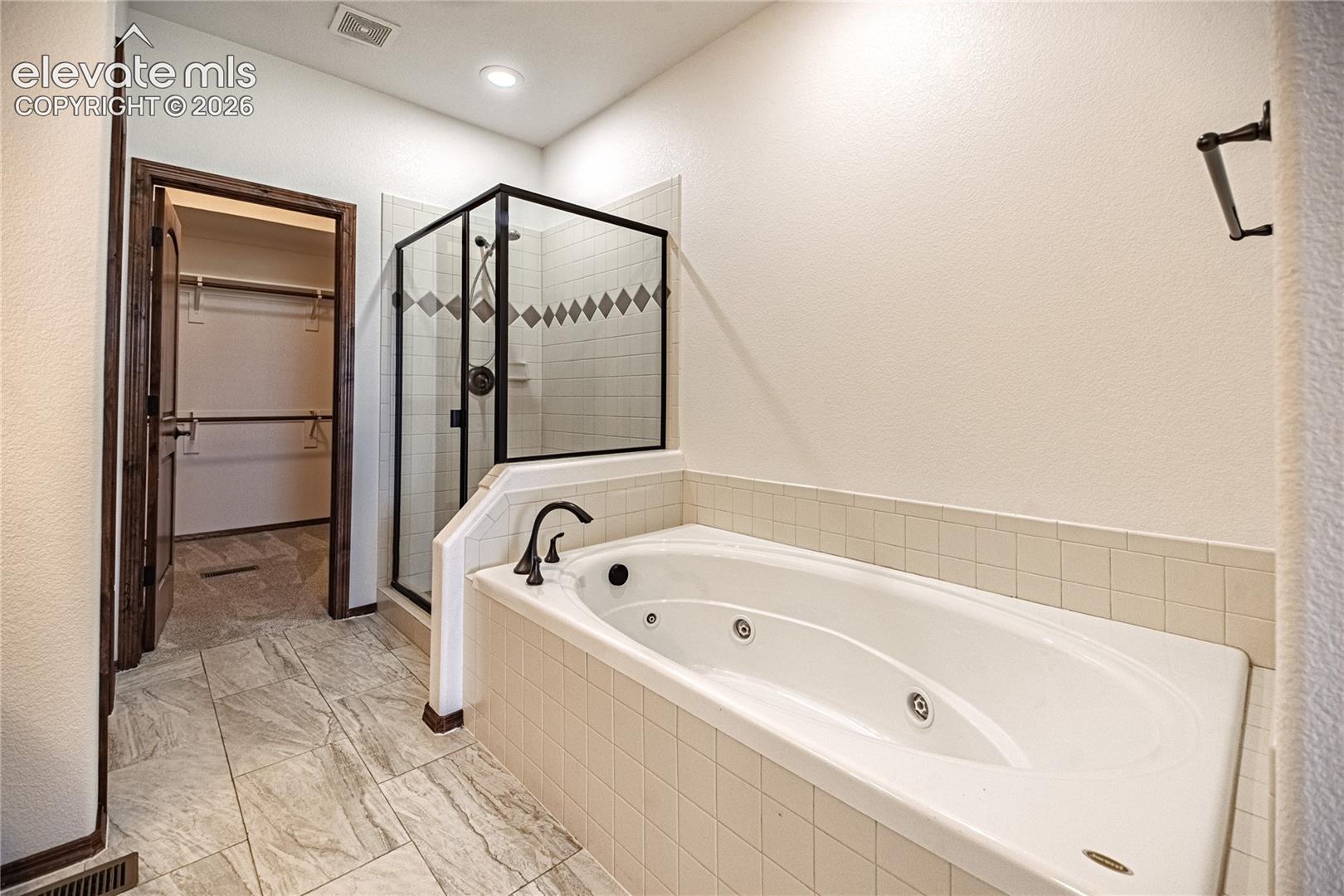 Soaking tub with tiled surround, walk-in shower with glass enclosure and decorative tile, and wood-finish flooring