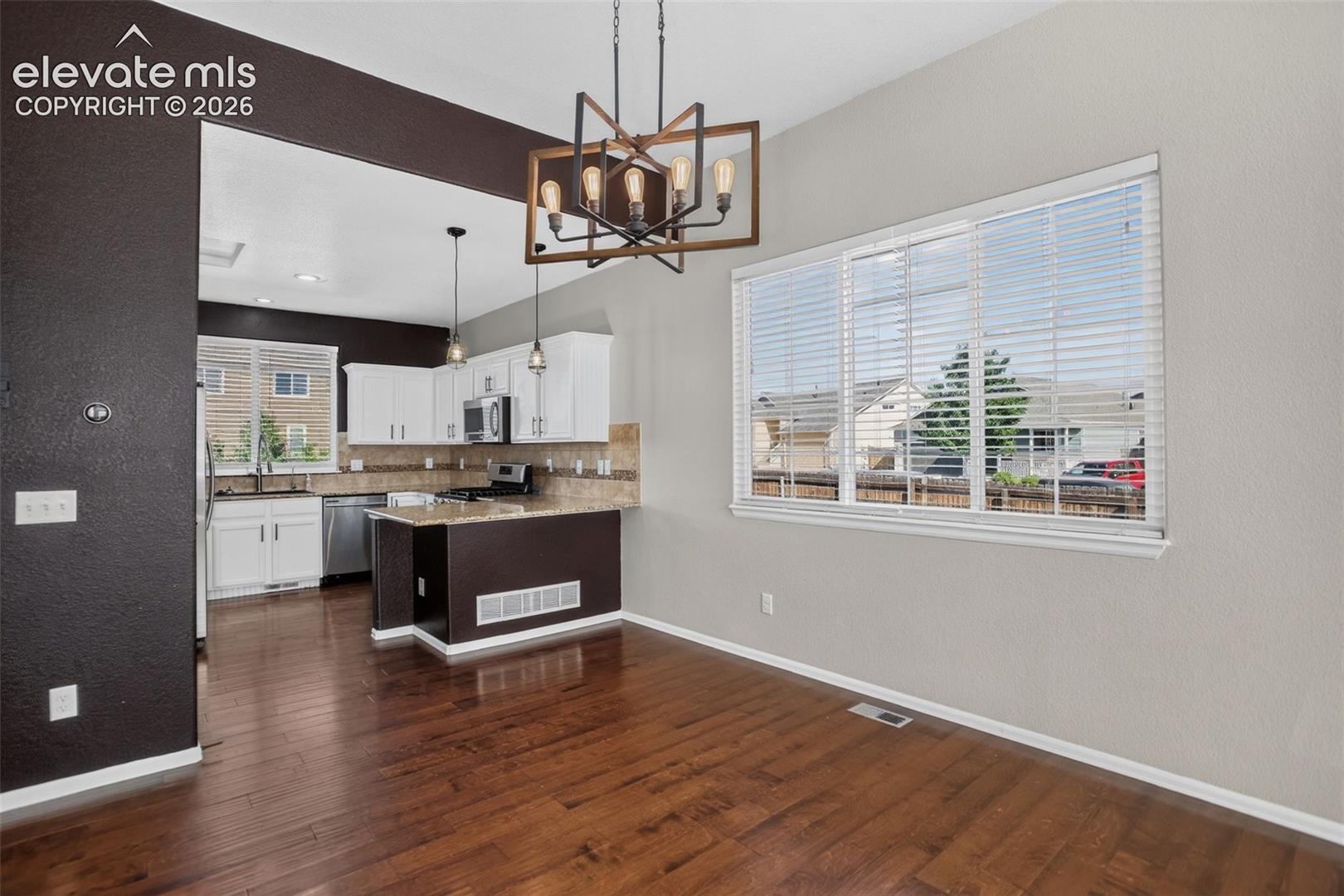 Wood-finish flooring throughout, framed window with blinds, and a kitchen featuring white cabinetry, stainless steel appliances, and a built-in island