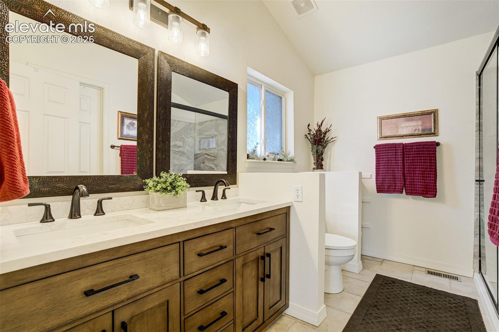 Dual-sink vanity with a stone countertop, dark wood-finish cabinetry, two framed mirrors, and a three-light fixture