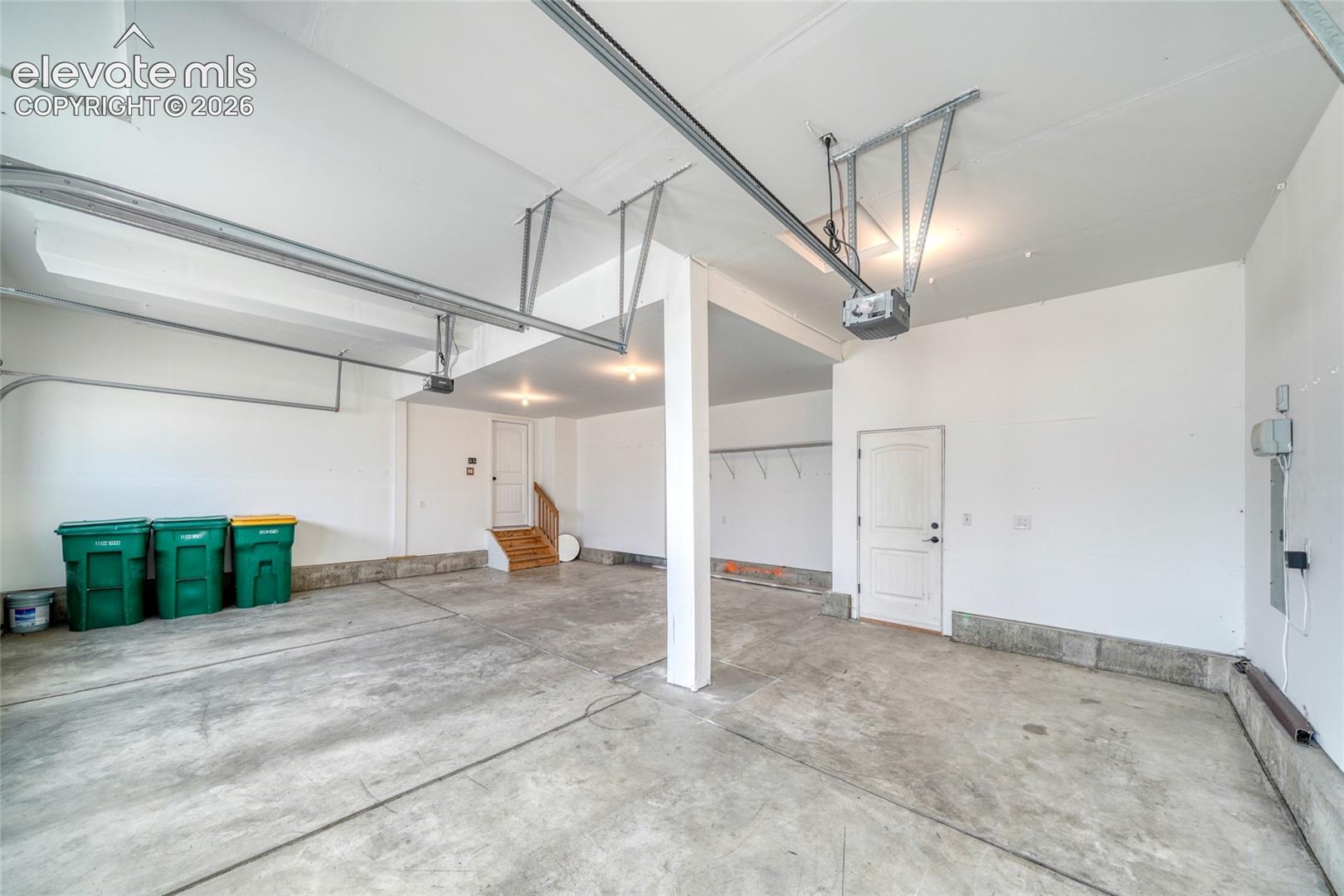 Spacious garage with concrete flooring, automatic garage door opener, overhead lighting, and built-in shelving