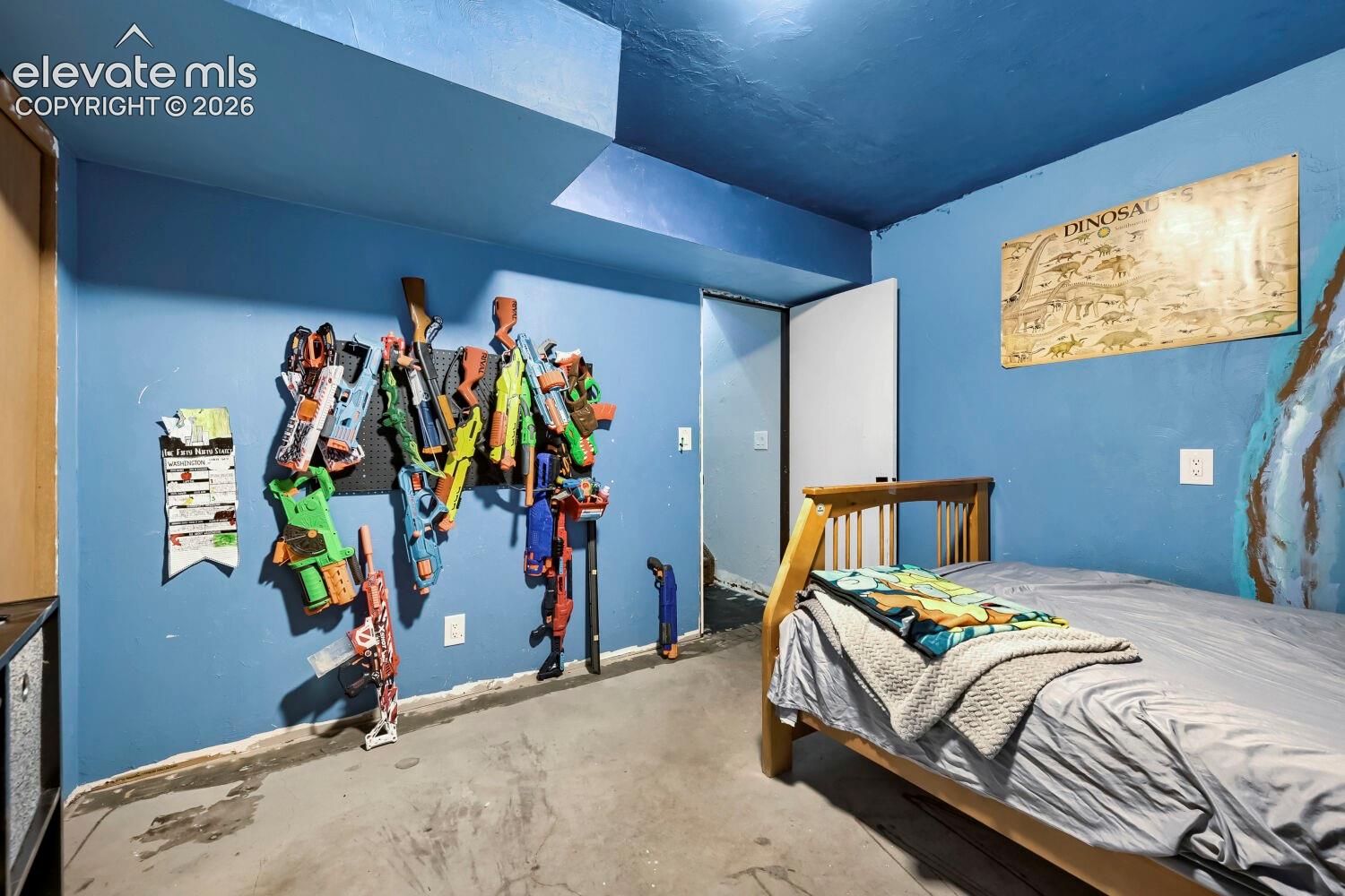 Room featuring blue painted walls and ceiling, a built-in wall-mounted storage system, a white interior door, a wooden bed frame, and concrete flooring