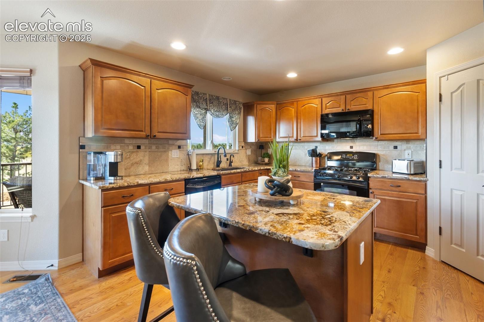 Kitchen featuring wood cabinetry, stone countertops, central island, natural wood-finish flooring, and integrated black appliances