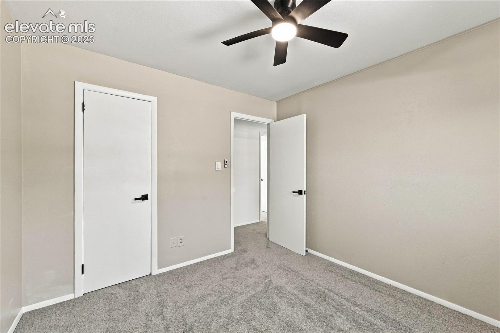 Plush gray carpeting, neutral wall palette, modern ceiling fan with integrated lighting, white trim, and doors with matte black hardware