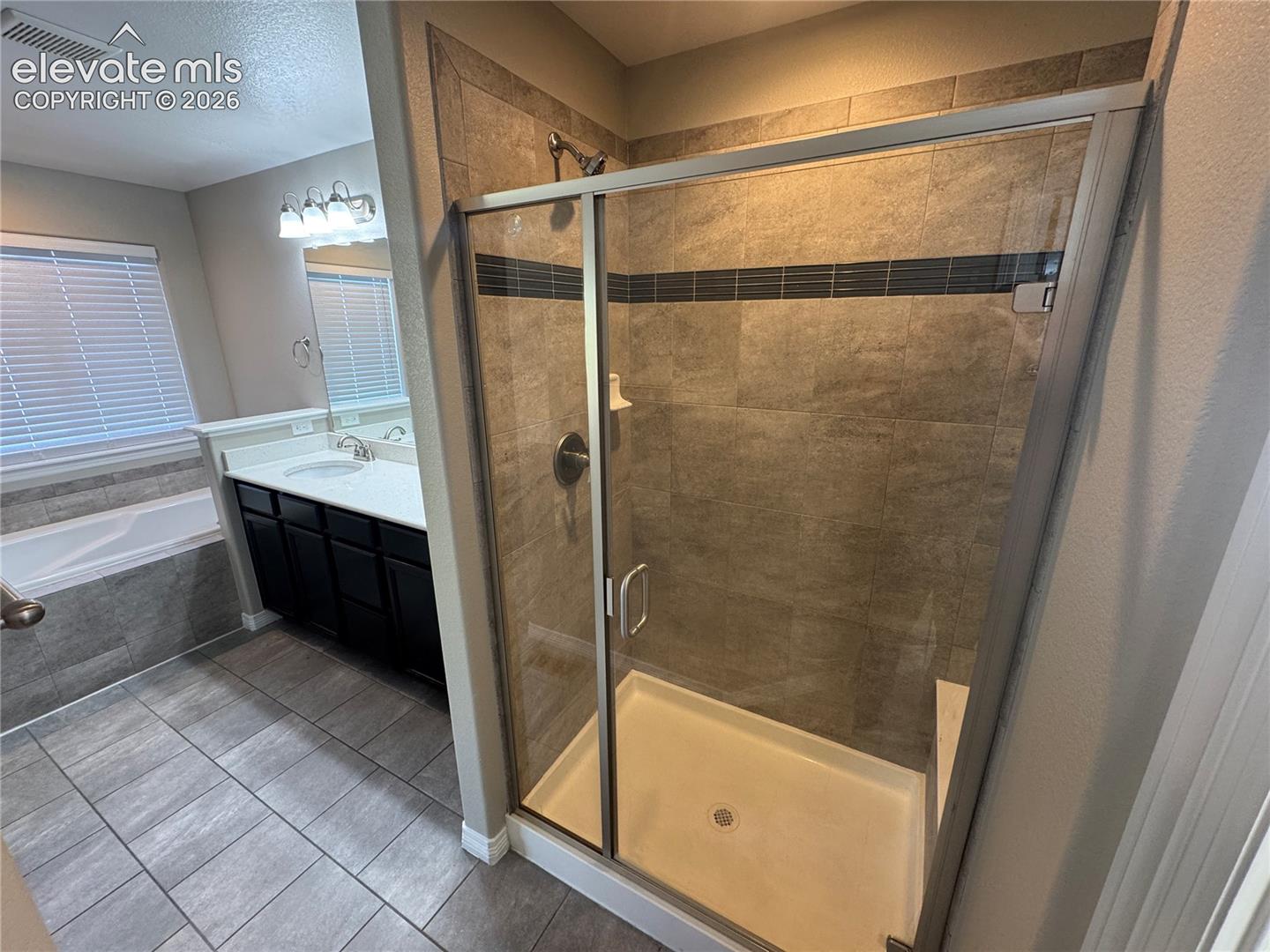 Shower stall featuring tile surround with decorative inlay, glass enclosure, and built-in bench, complemented by dark-finish cabinetry with a white countertop and tile flooring