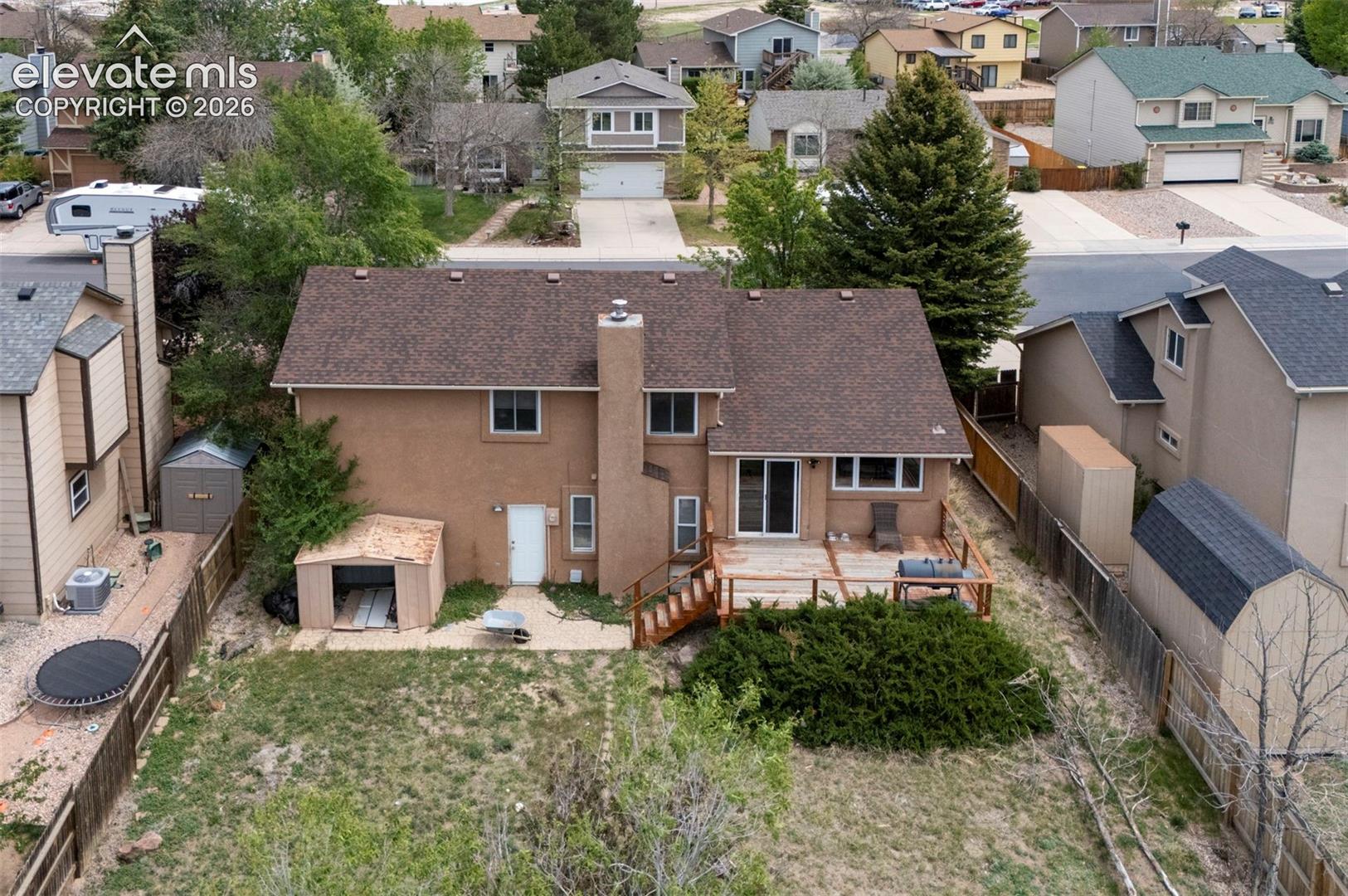 Rear exterior featuring a spacious deck with perimeter railing, ground-level patio access, and a stucco finish