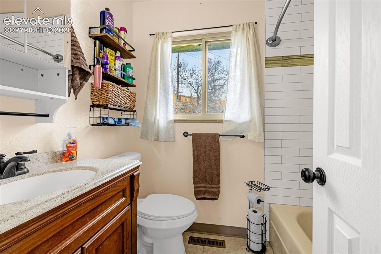 Bathroom featuring a wood-finish vanity with a stone-composite countertop, subway tile shower surround, and a wall-mounted mirrored medicine cabinet