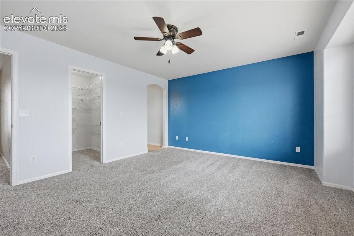 Spacious room featuring plush carpet flooring, a ceiling fan, and a walk-in closet with wire shelving