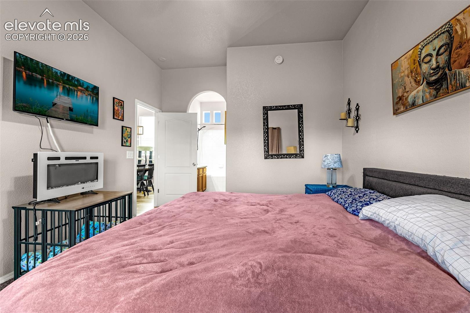 Room featuring vaulted ceilings, a prominent arched doorway, neutral wall finishes, and a wall-mounted hardwired electrical fixture