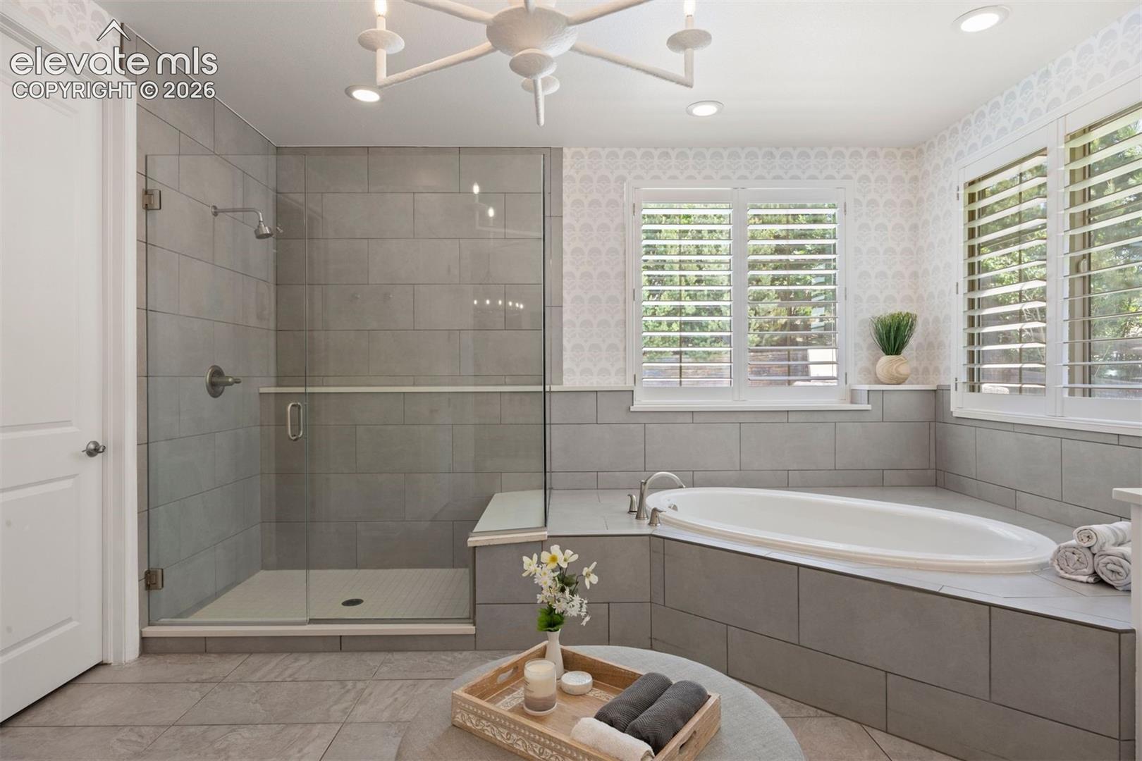 Bathroom featuring an oval drop-in soaking tub and a glass-enclosed shower with a built-in bench