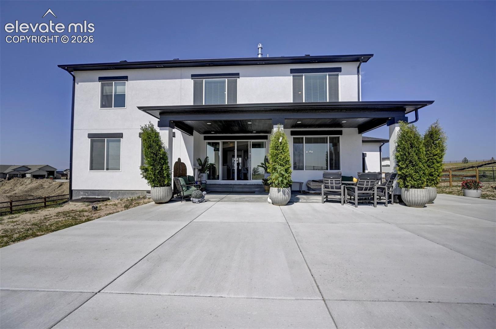 White stucco exterior with black trim, featuring a covered patio, extensive concrete hardscaping, and large windows