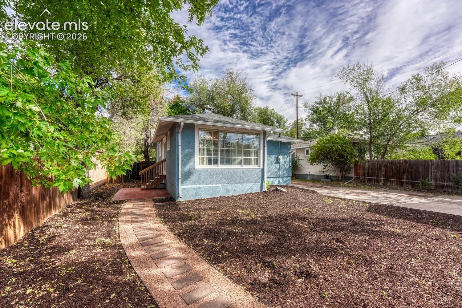 Exterior featuring a stucco finish, multi-pane windows, a fenced perimeter, a paved pathway, and a gravel driveway