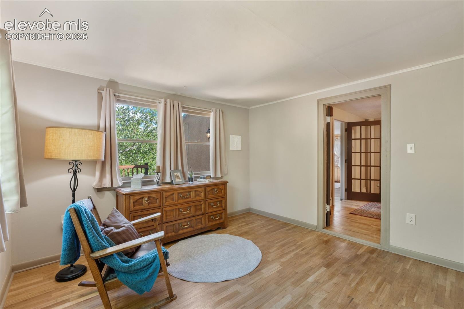 Light wood-finish flooring extends through this room featuring two windows with natural light, a neutral wall color, and white baseboards and crown molding