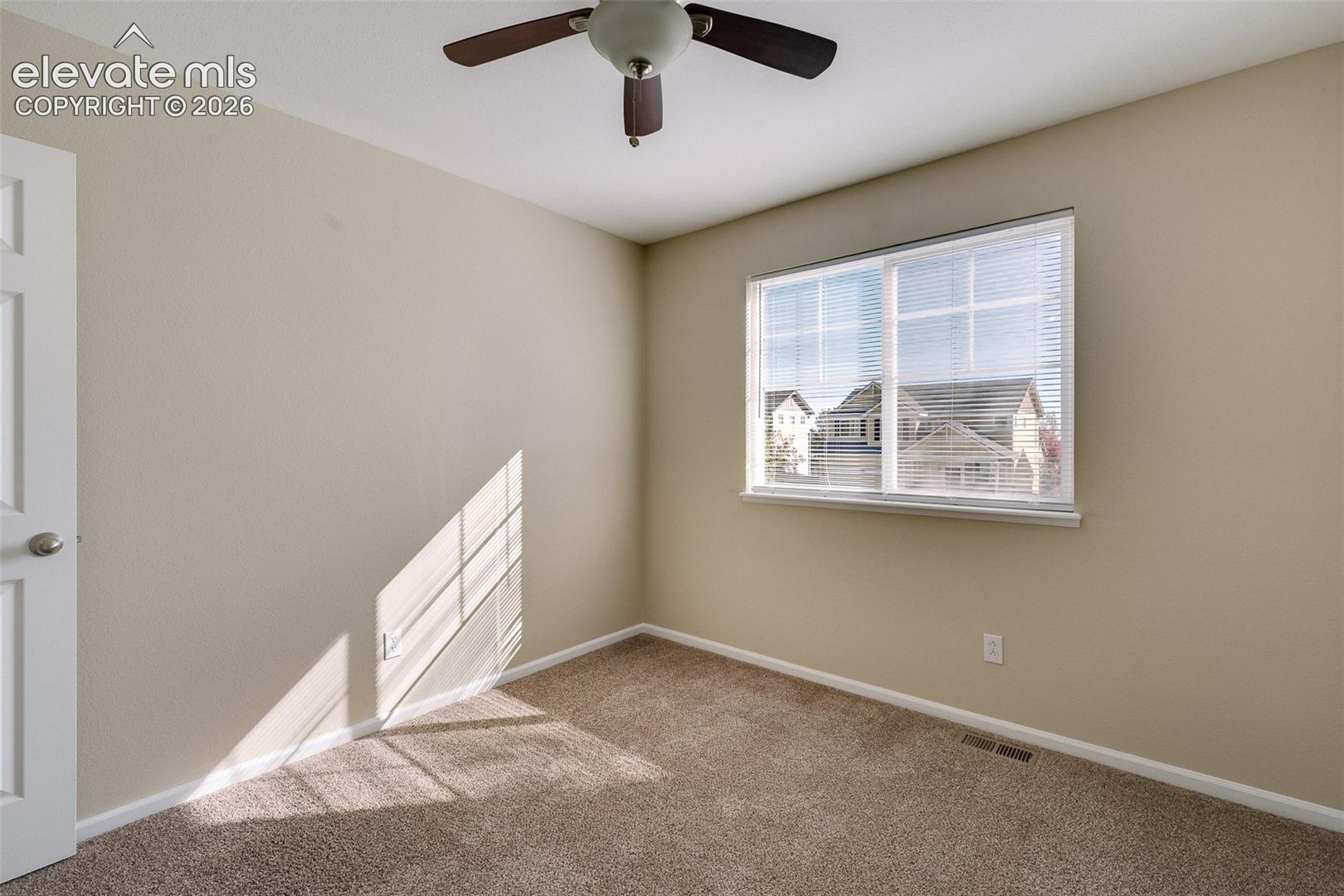 Neutral-toned interior featuring wall-to-wall carpeting, a multi-pane window with horizontal blinds, and a ceiling-mounted fan with integrated lighting