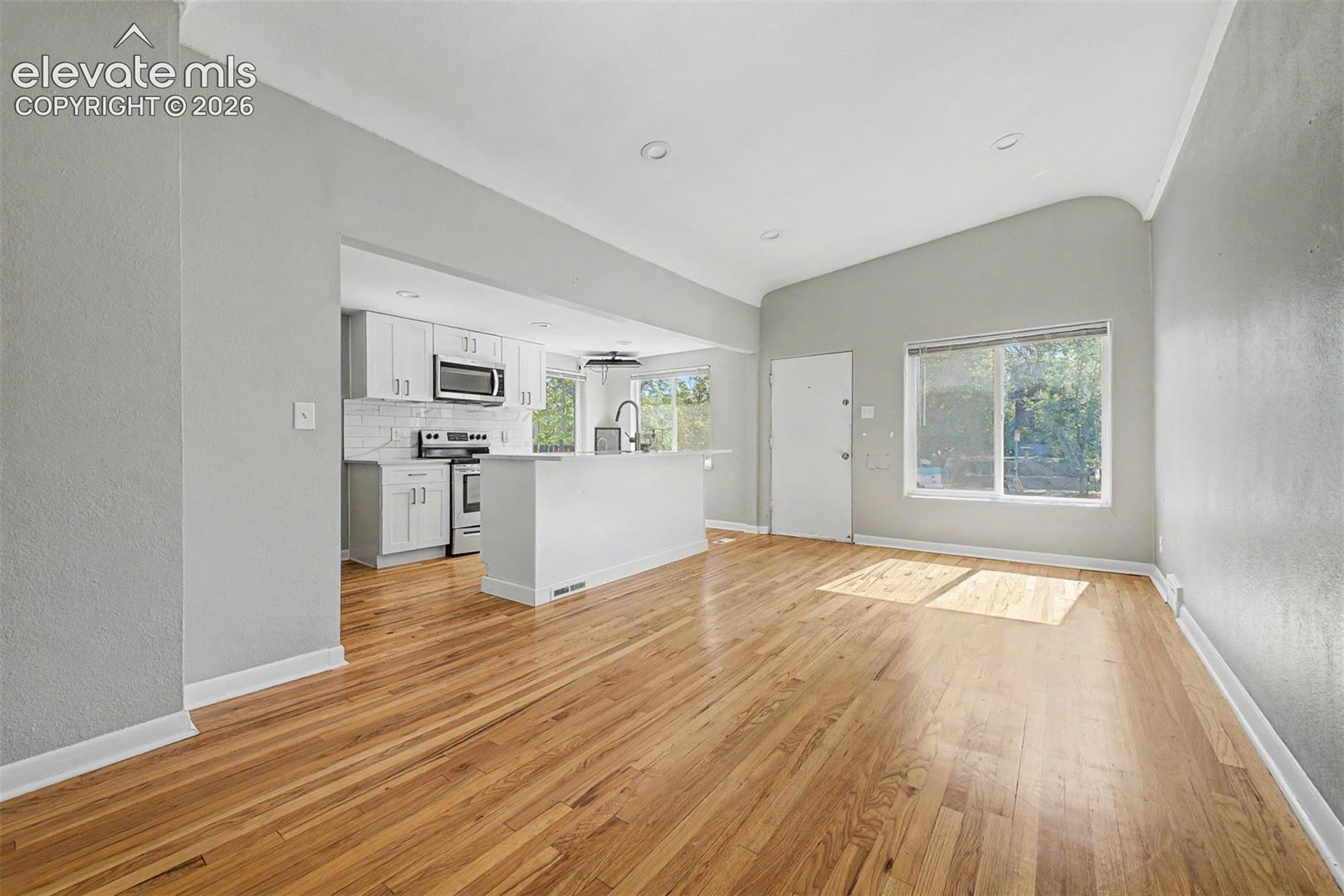 Modern kitchen featuring wood-finish flooring, white cabinetry with gold-tone hardware, stainless steel appliances, white countertops, and a white subway tile backsplash