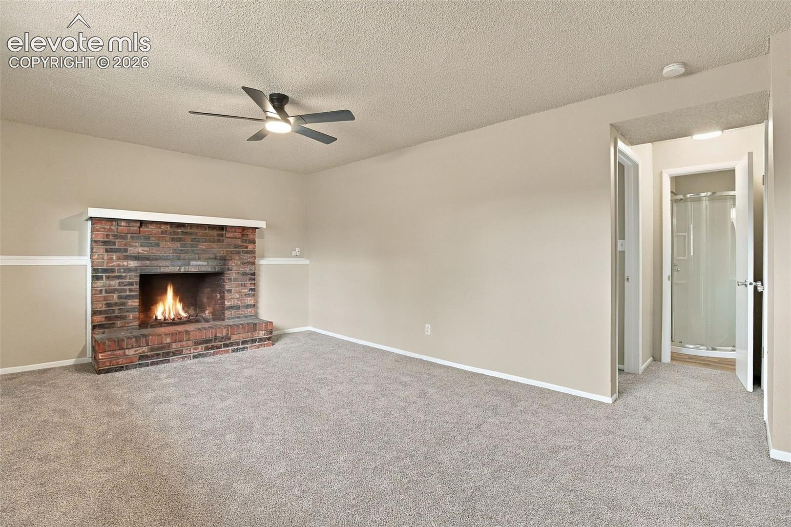 Living area featuring a floor-to-ceiling brick fireplace, neutral carpeting, ceiling fan with integrated lighting, and chair rail molding