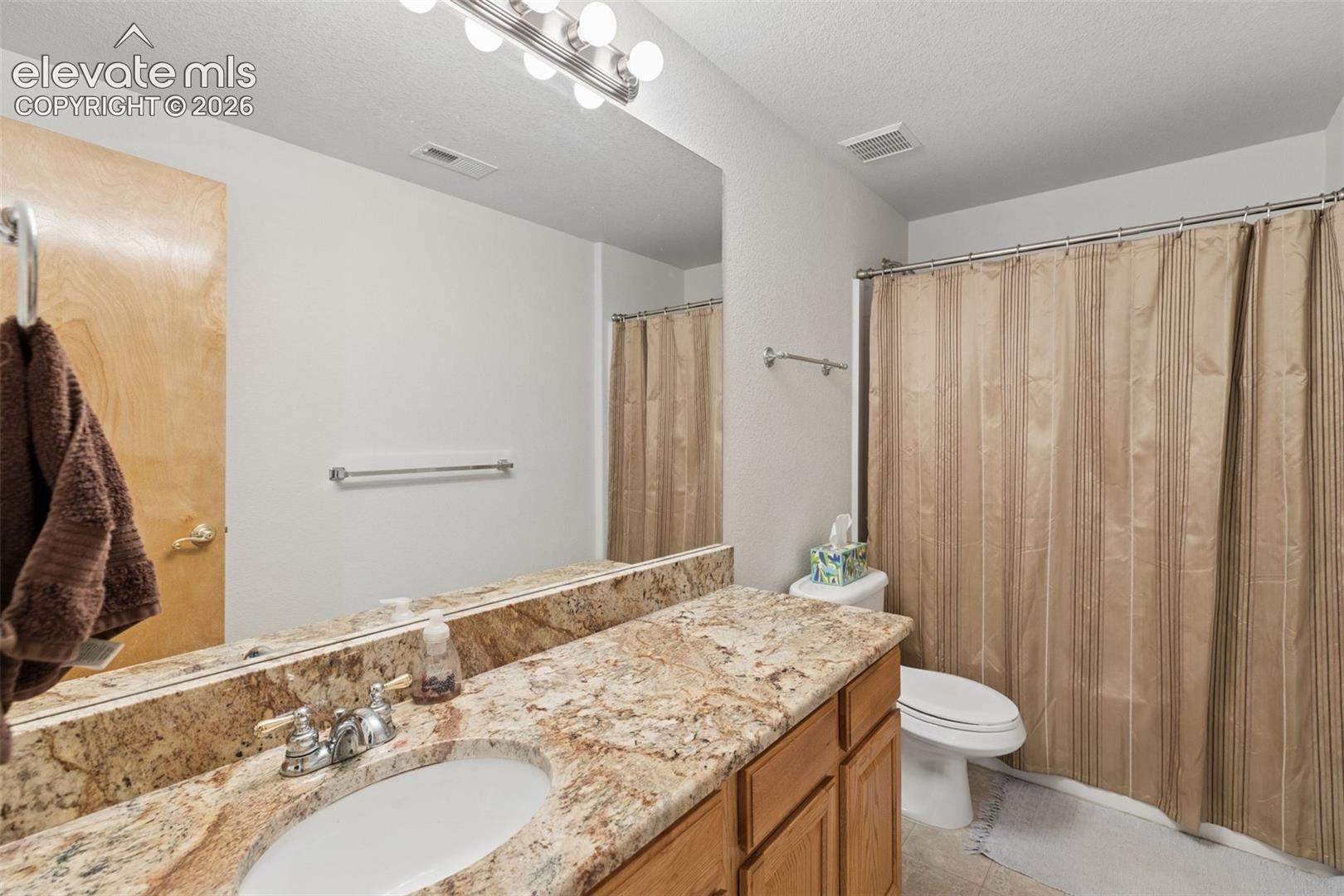 Bathroom featuring stone-surface countertop, wood-finish cabinetry, undermount sink with chrome hardware, and wall-mounted vanity lighting