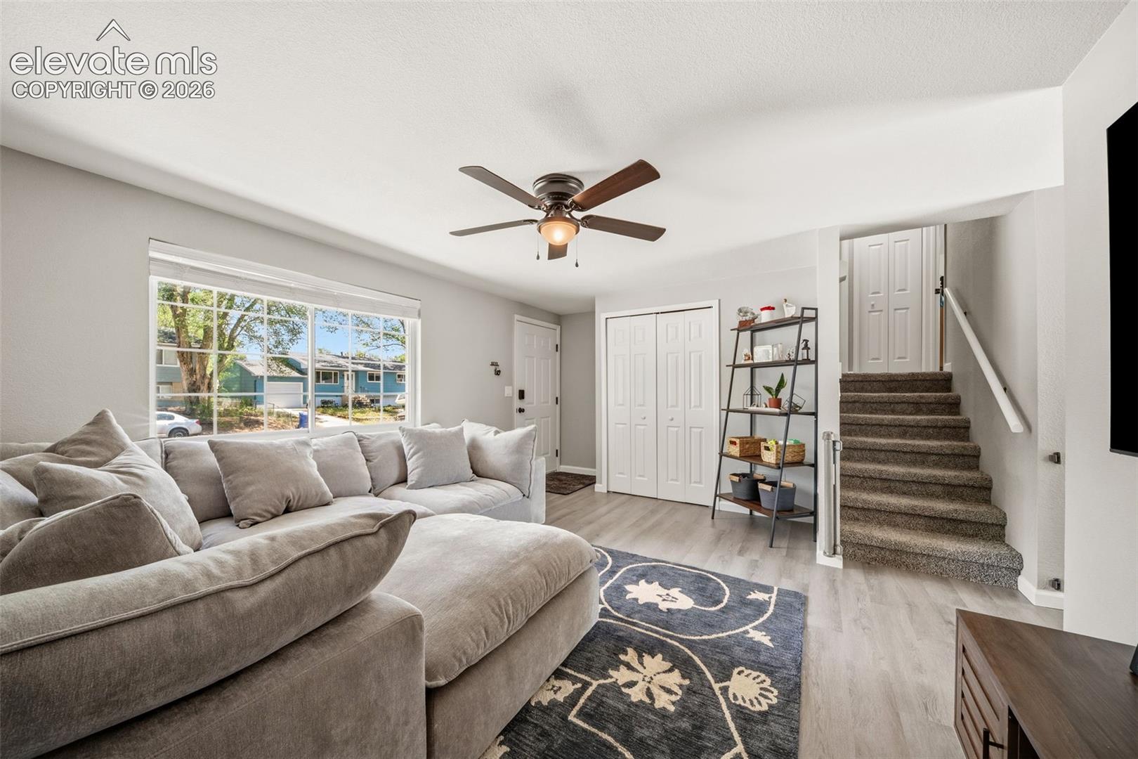 Wood-finish flooring, ceiling fan, and staircase with carpeted treads