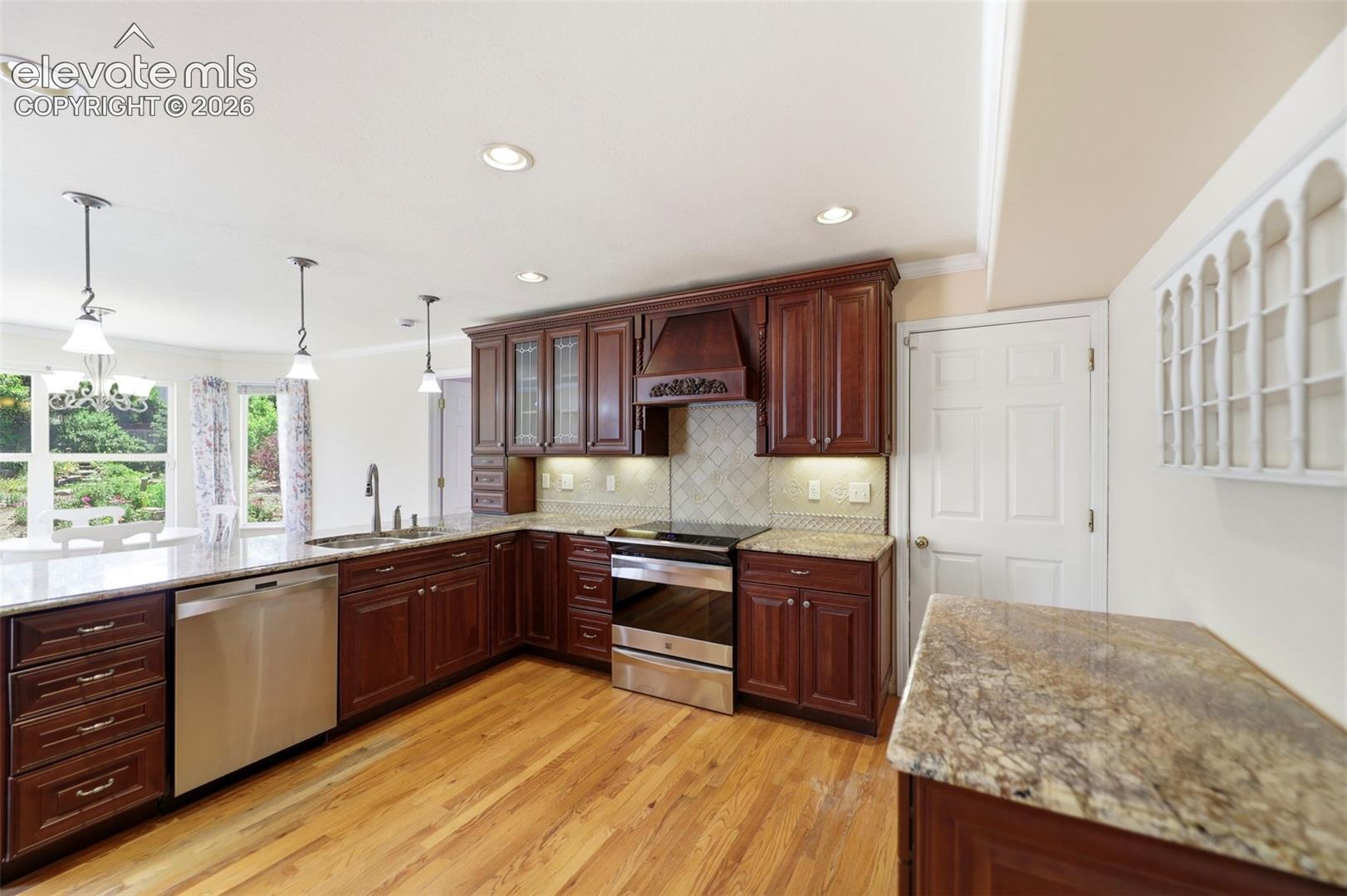 Kitchen featuring rich wood cabinetry, granite countertops, stainless steel appliances, wood-finish flooring, and recessed lighting