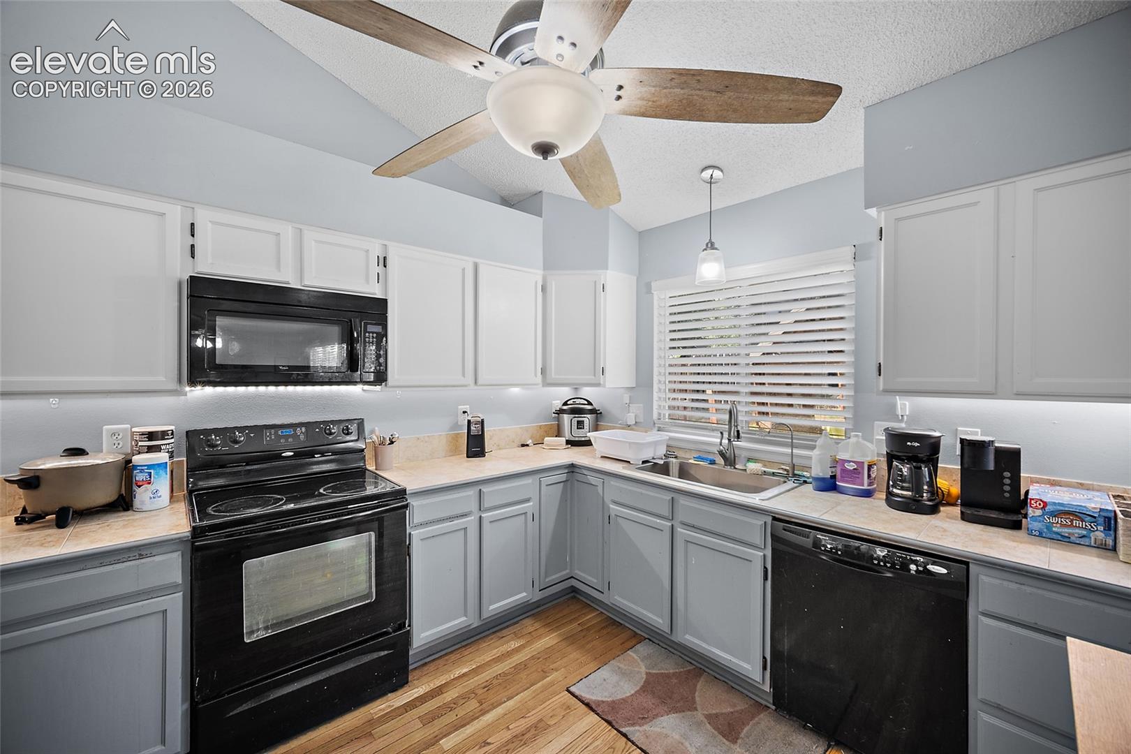 Kitchen featuring wood-finish flooring, two-tone cabinetry, a ceiling fan with integrated lighting, and built-in appliances