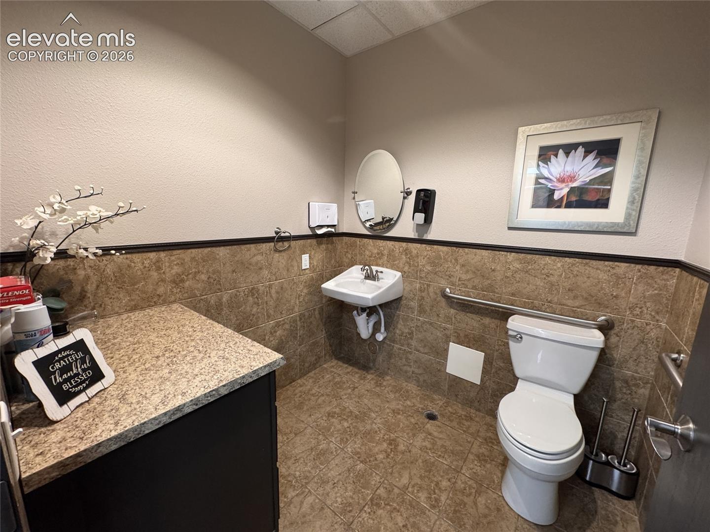 Wall-mounted sink, toilet with grab bar, built-in lower cabinetry with countertop, and tile flooring
