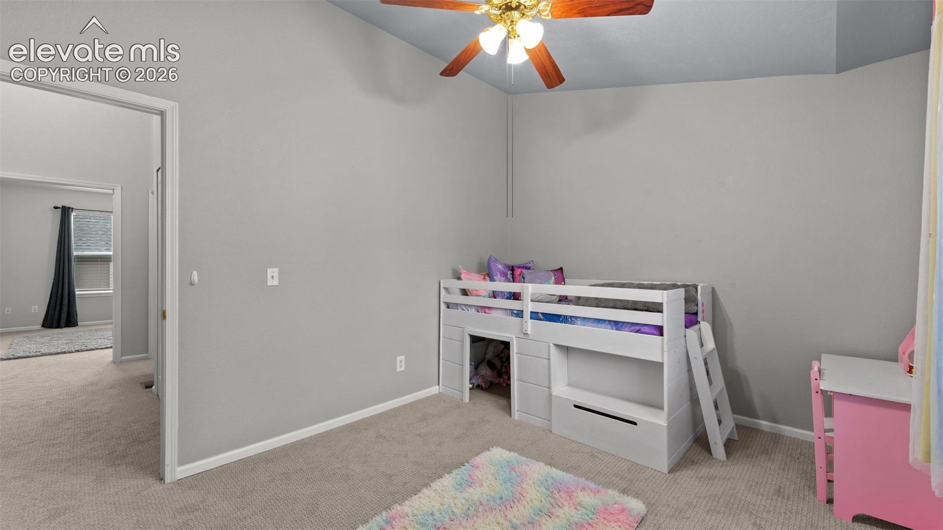 Vaulted ceilings featuring a central ceiling fan with integrated lighting, neutral wall tones, and neutral carpeting