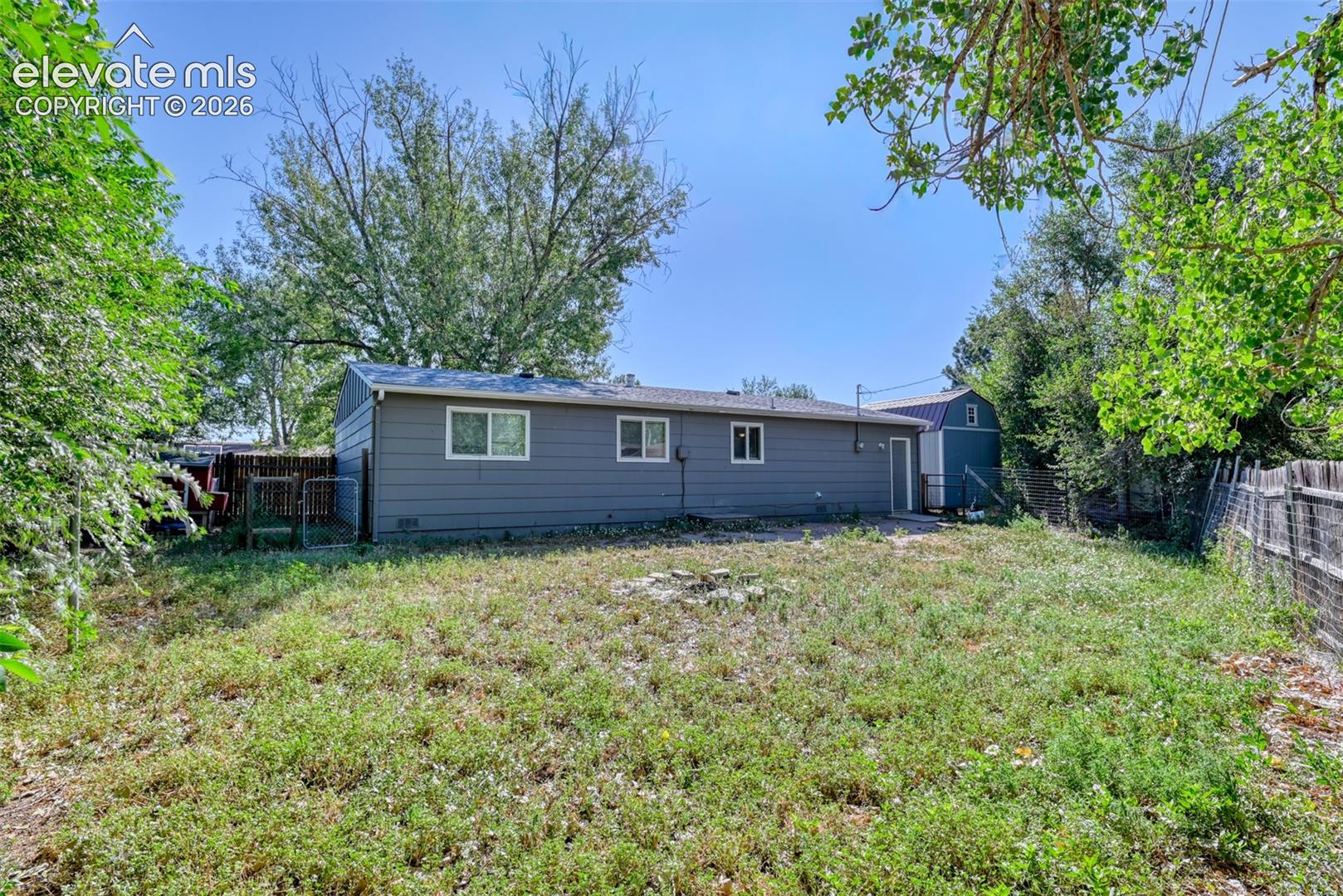 Expansive backyard featuring a gray siding exterior, multiple windows, a rear entry door, and perimeter fencing