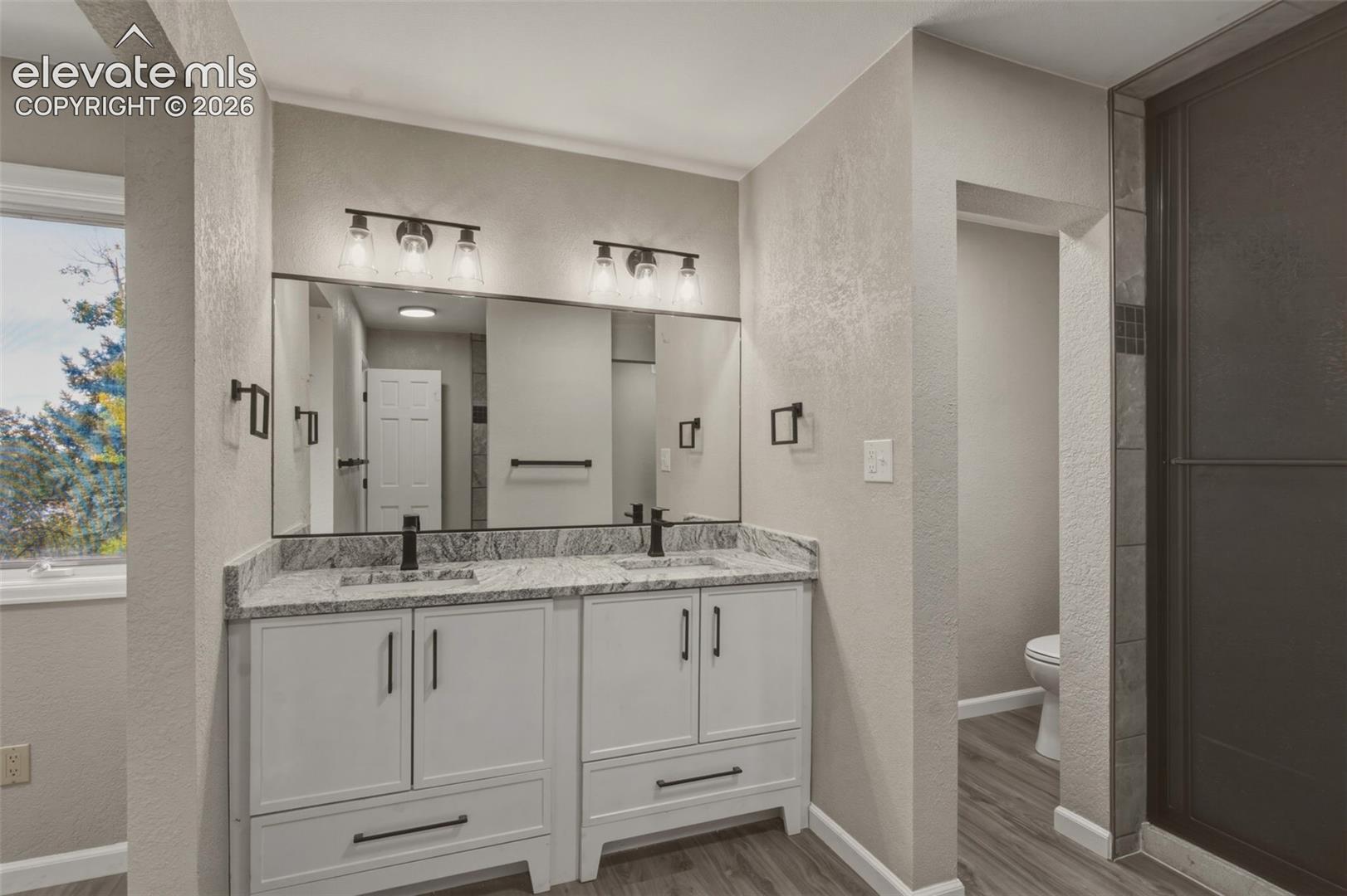 Dual vanity with stone-finish countertop, wood-finish flooring, framed mirror, and matte black fixtures