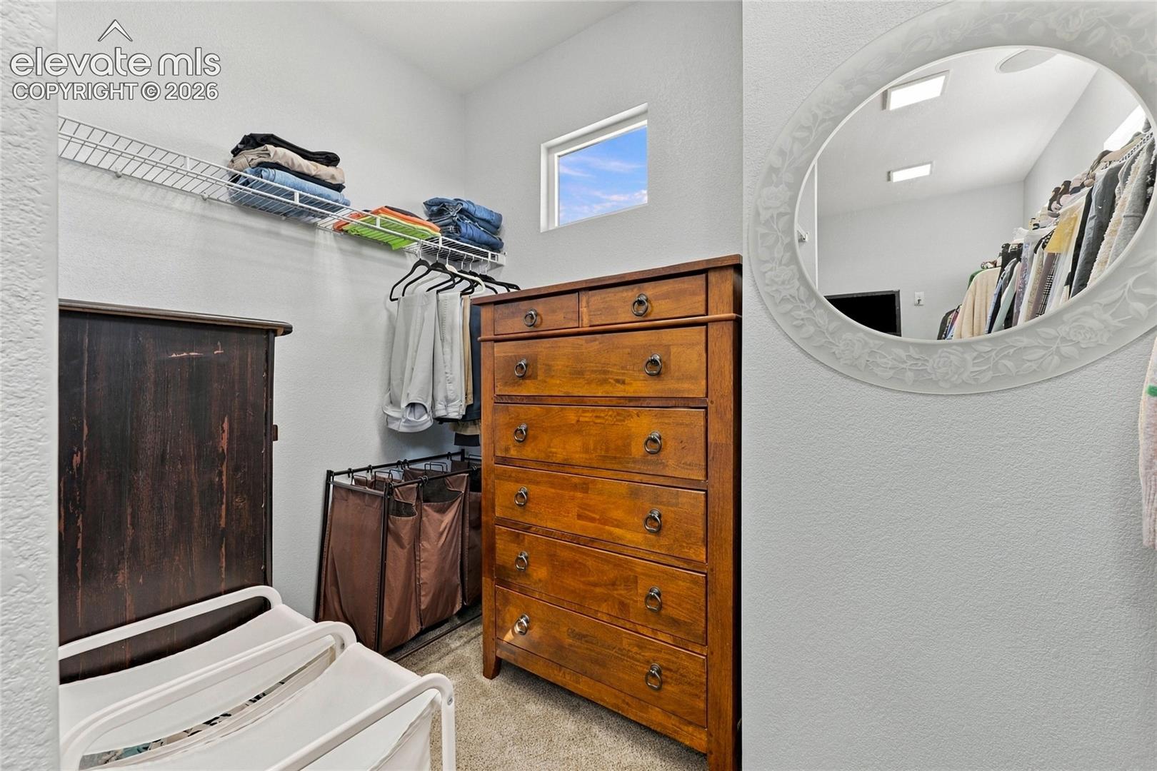 Storage area featuring wire shelving, a wall-mounted oval mirror, and a window