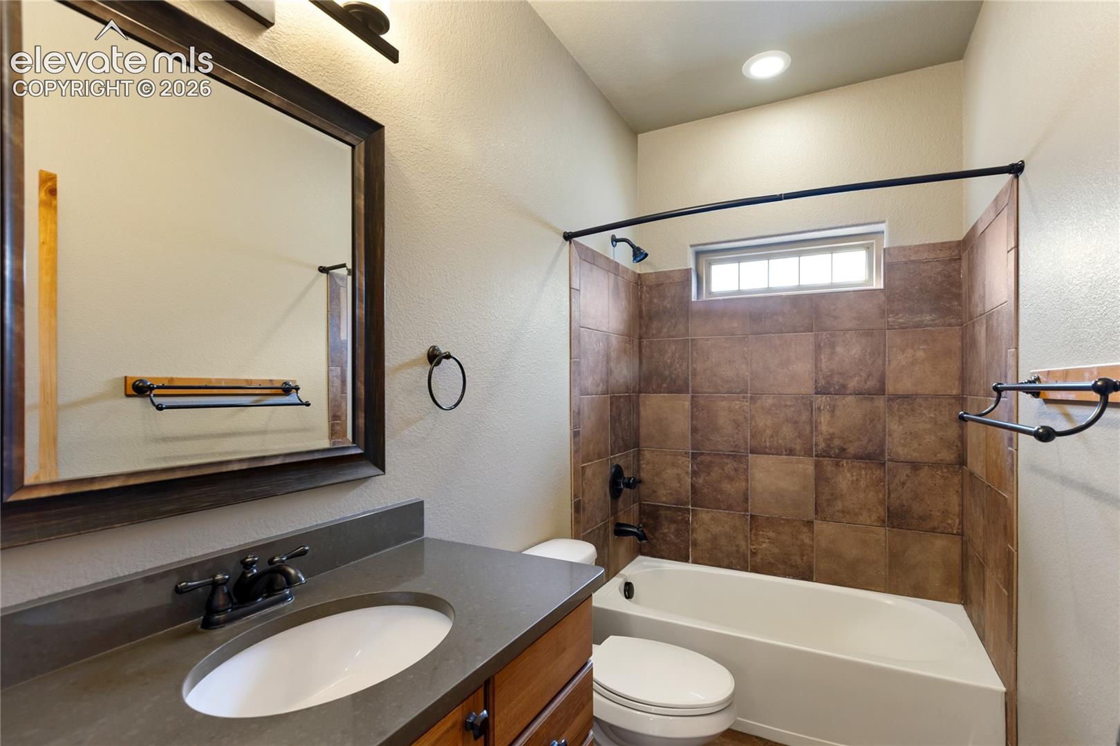 Bathroom featuring a dark wood-finish vanity with a stone countertop, an integrated oval sink, square-tile shower surround, and a matte black shower fixture