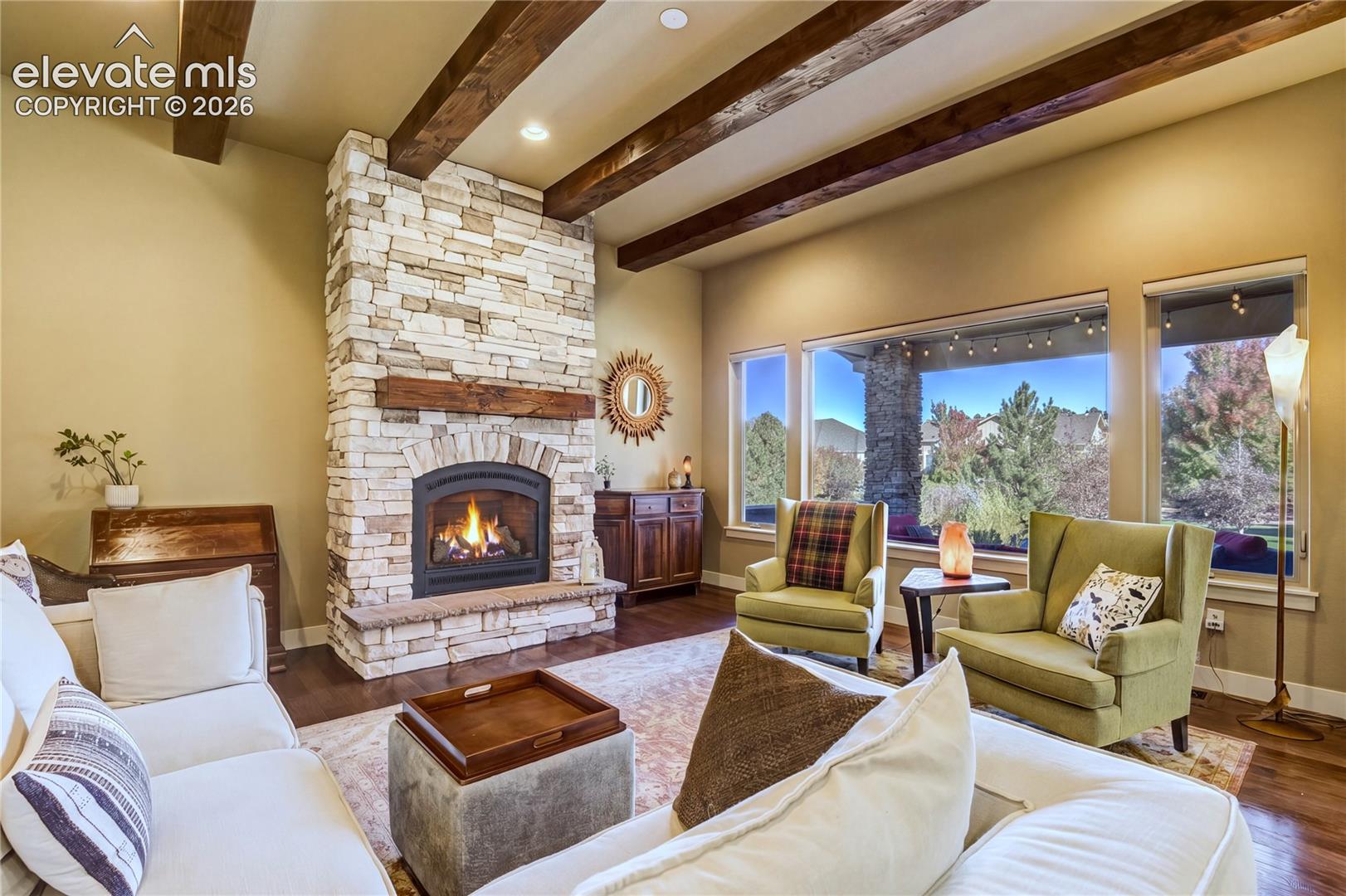A dramatic floor-to-ceiling stone fireplace anchors the Great Room, rising beneath an 11-foot ceiling accented by substantial knotty alder beams. Generous windows invite natural light + views of the surrounding landscape.