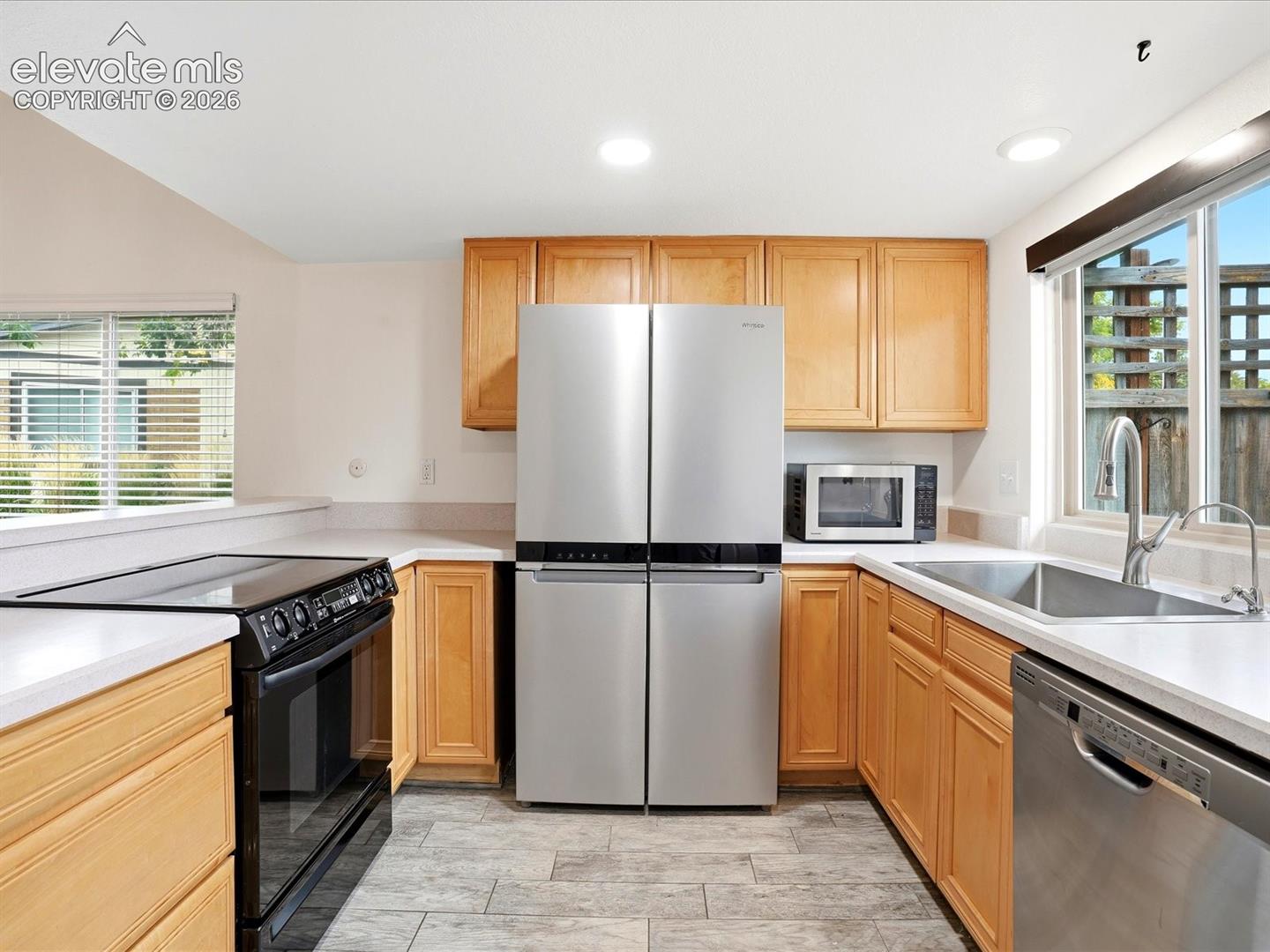 Kitchen featuring wood cabinetry, stainless steel appliances, solid surface countertops, tile flooring, and a stainless steel undermount sink with a pull-down faucet
