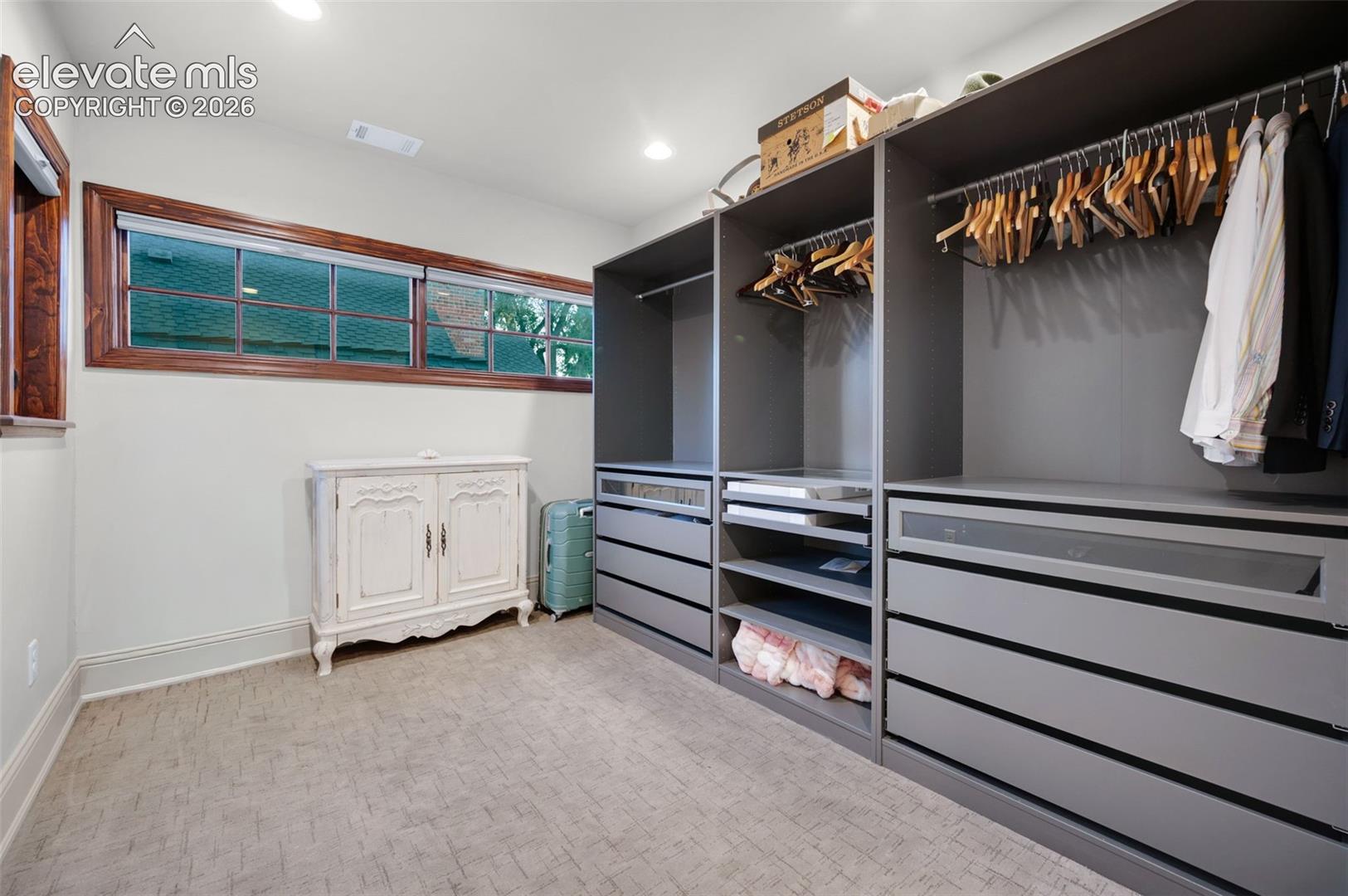 Walk-in closet featuring extensive dark grey custom cabinetry, integrated shelving, tiered storage drawers, and recessed lighting