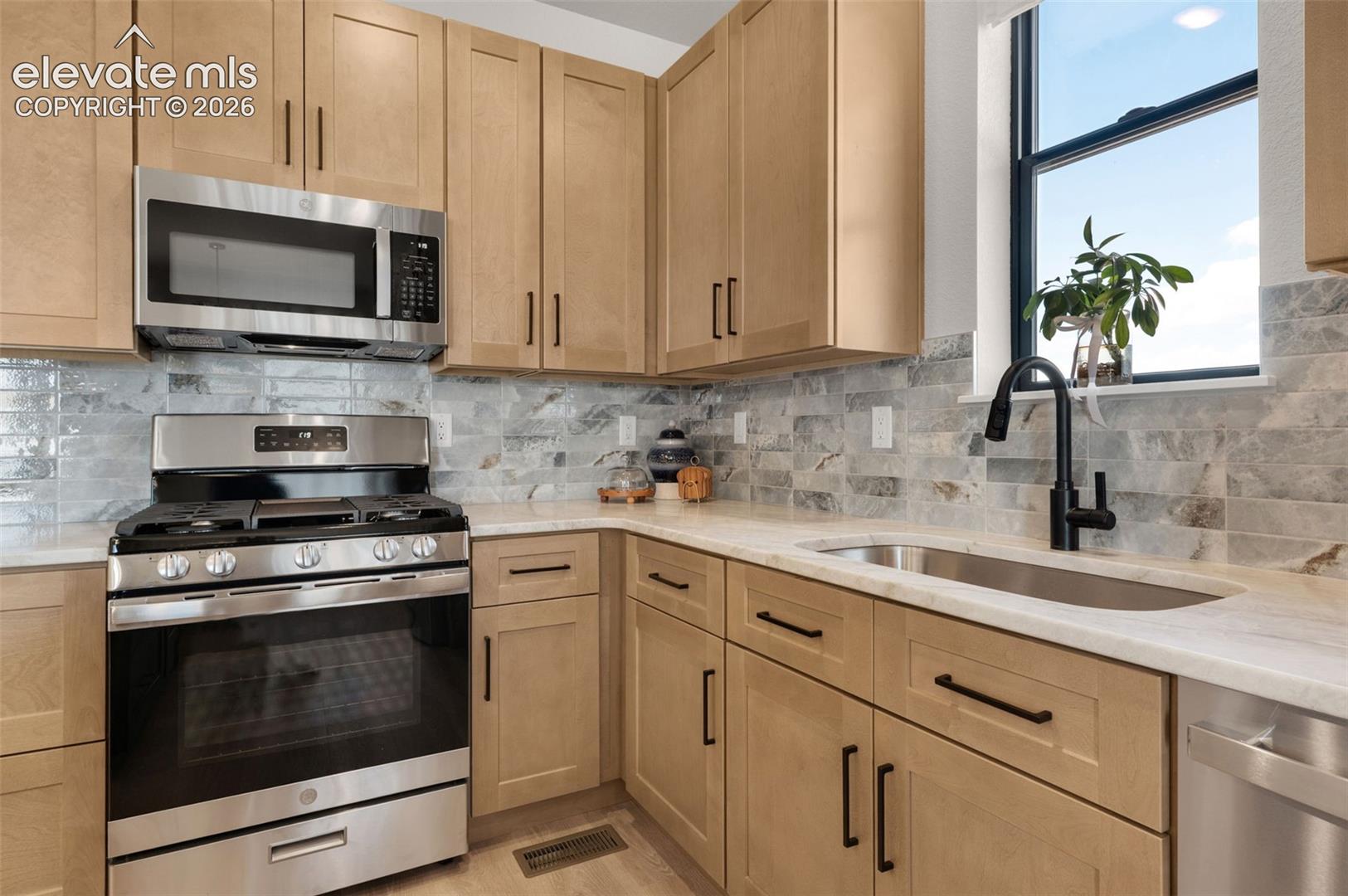 Light-toned cabinetry with matte black hardware, stainless steel appliances, light-toned countertops, and a subway tile backsplash