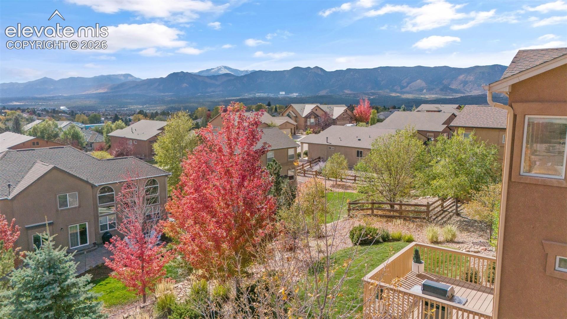 Elevated perspective featuring mountain scenery, mature trees, tiered deck, and fenced rear grounds