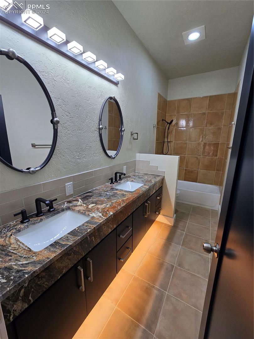 Bathroom featuring tile patterned flooring, vanity, tiled shower / bath combo, and backsplash