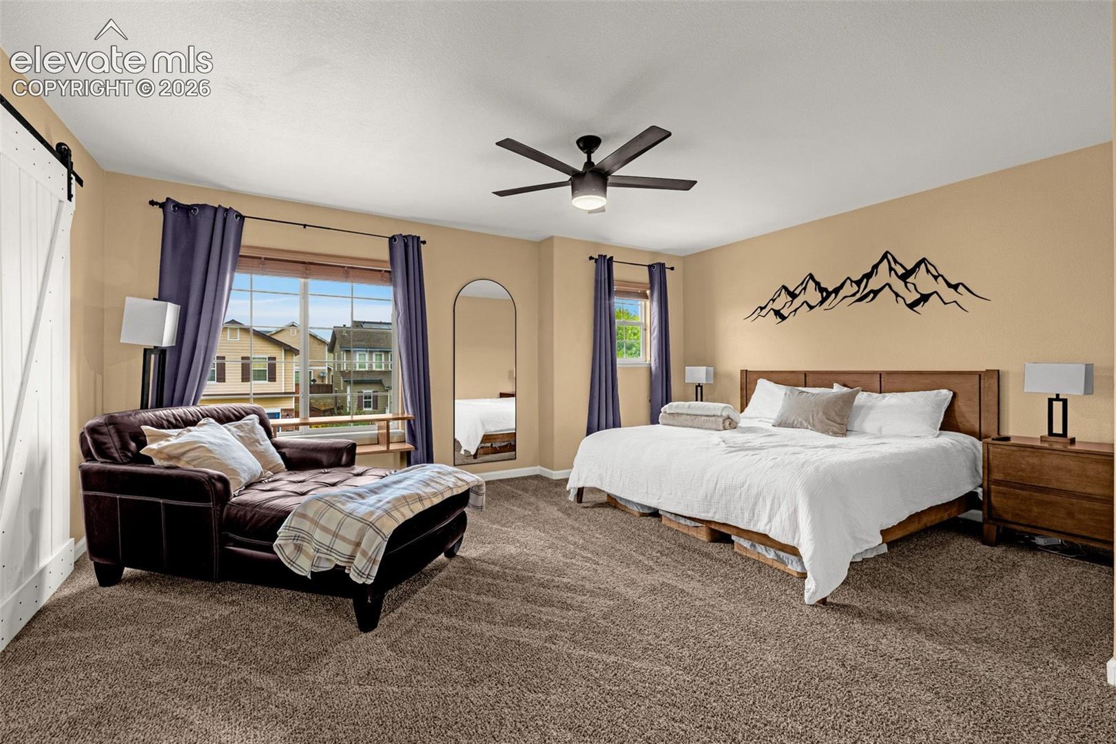 Room featuring wall-to-wall carpeting, a multi-blade ceiling fan, and a white sliding barn door