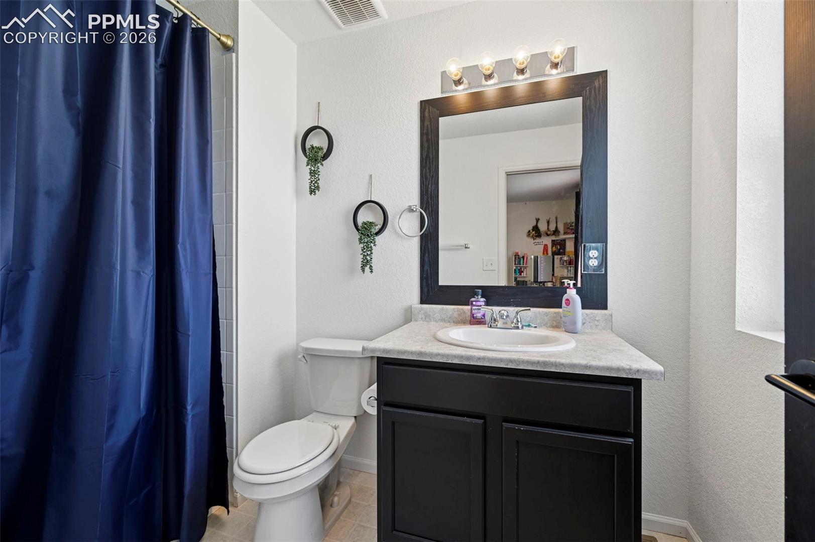 Bathroom featuring a white toilet, black vanity with a light-colored countertop and integrated sink, and a framed mirror with a four-bulb vanity light fixture