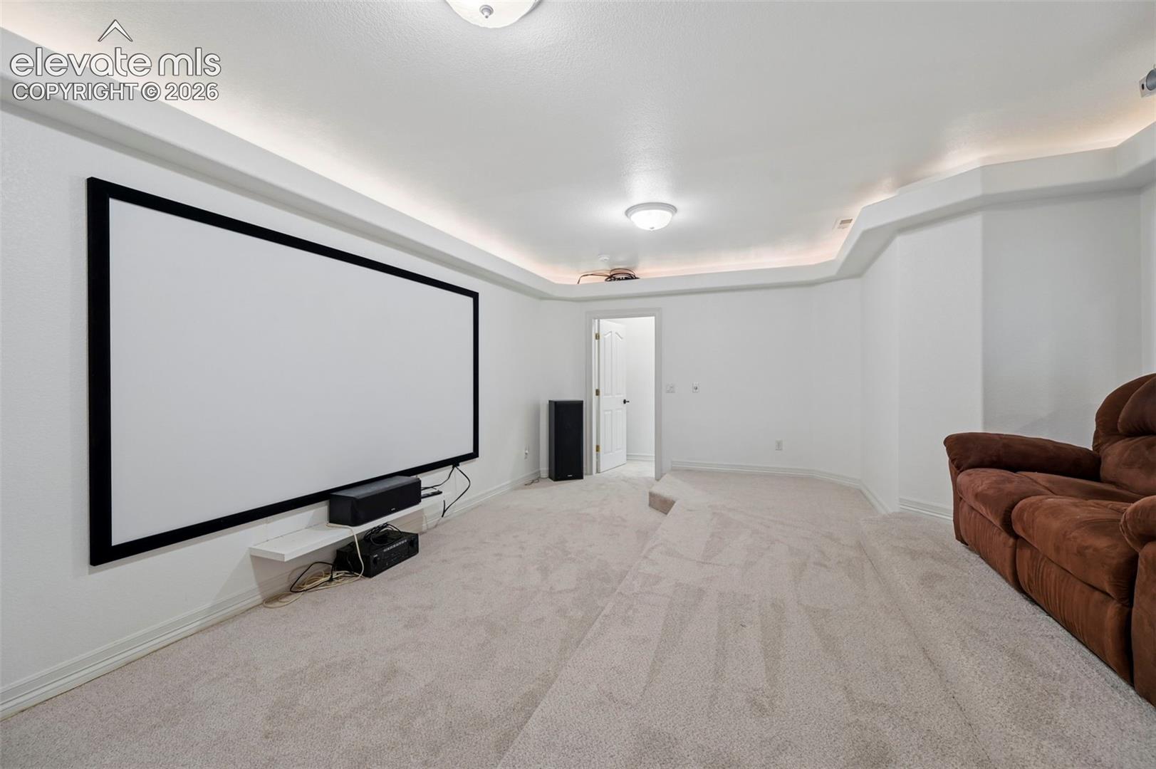 Dedicated media room featuring a large projection screen, recessed ceiling lighting, and light-toned carpeting
