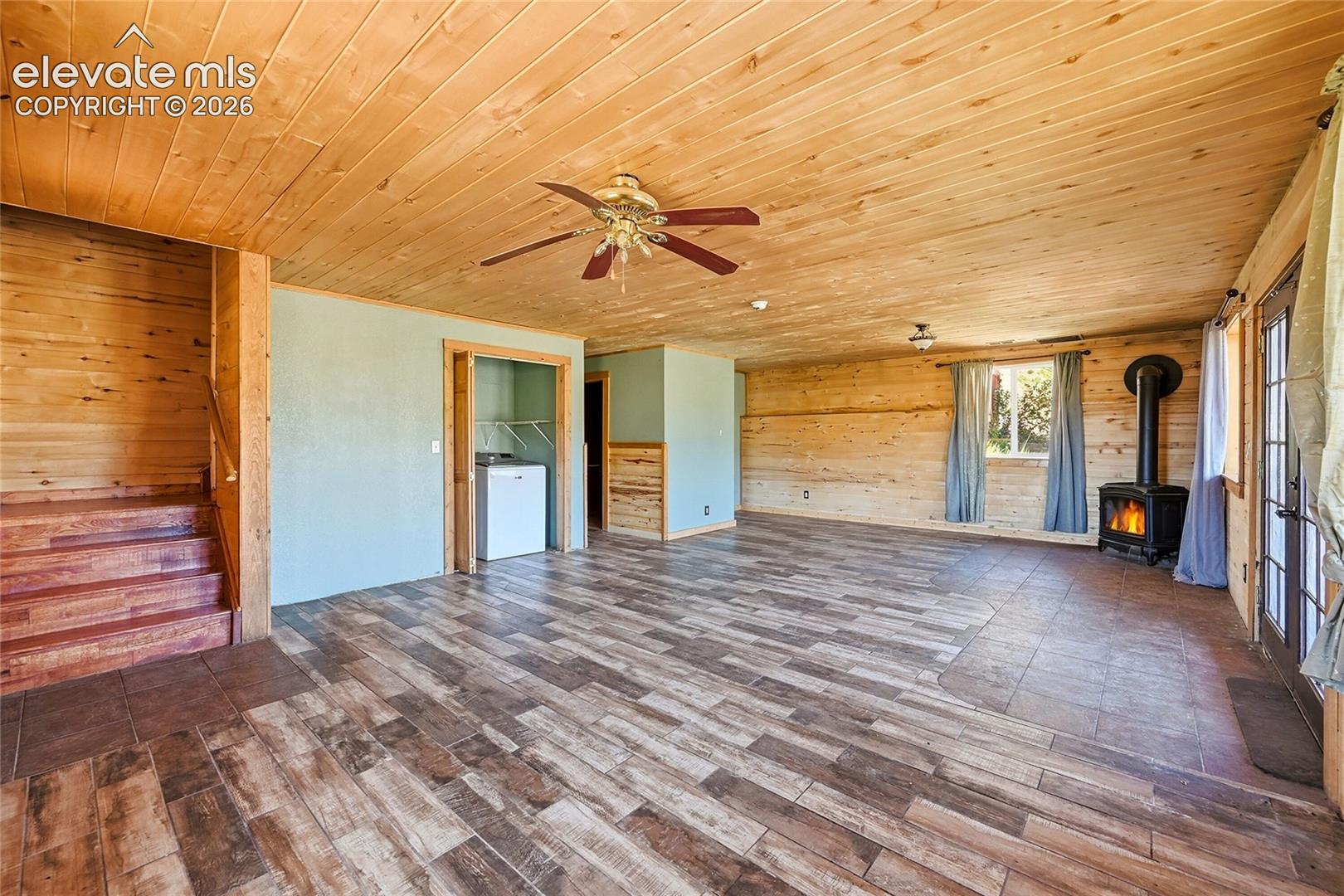 Wood-paneled ceiling, wood-finish flooring, wood-clad walls, wood-burning stove, and a ceiling fan