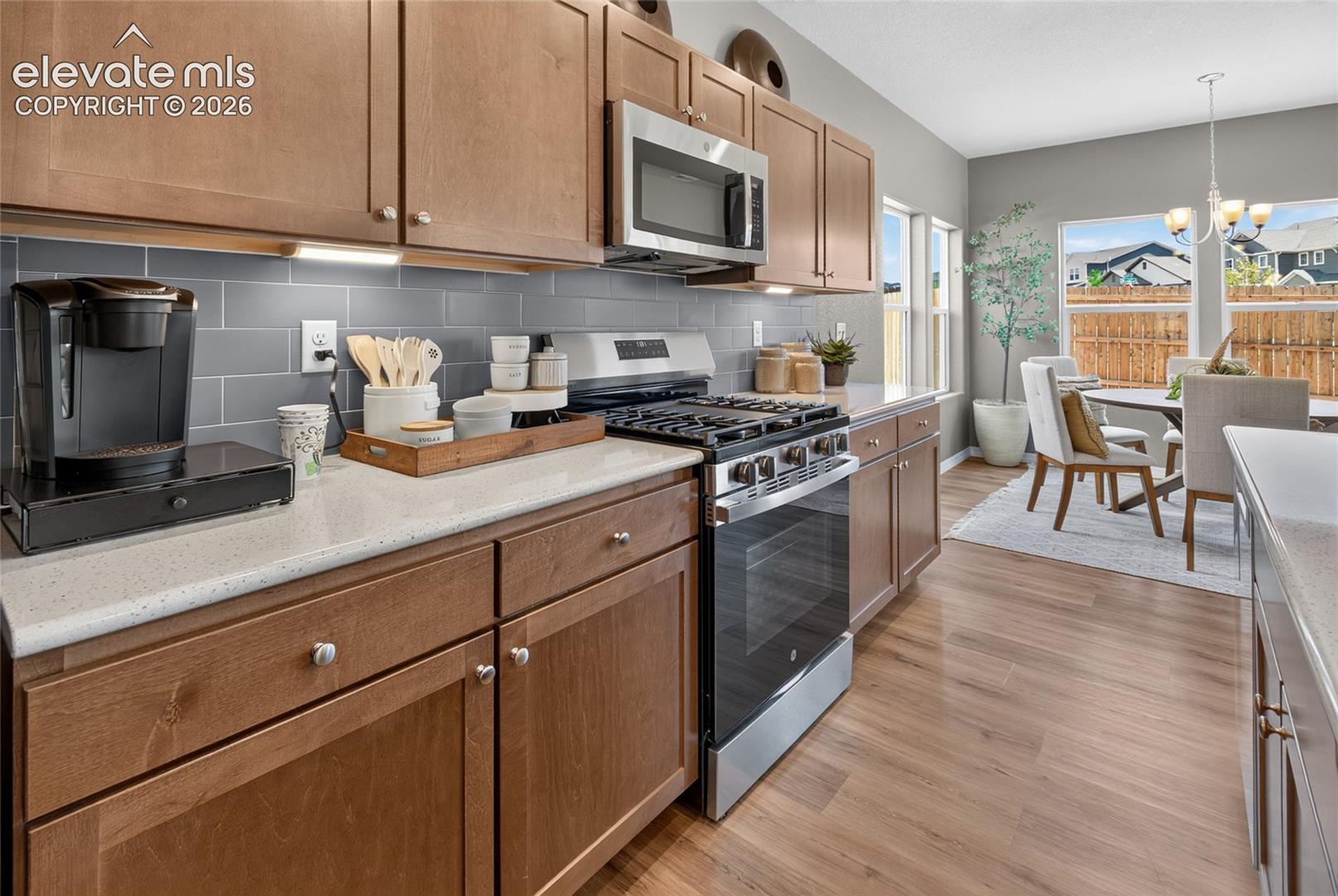 Kitchen featuring wood cabinetry, stone-finish countertops, grey subway tile backsplash, stainless steel gas range with microwave, and wood-finish flooring
