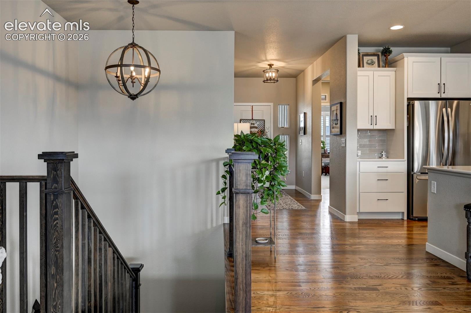 Hardwood flooring, dark wood newel posts, and balusters, with a contemporary spherical chandelier, and white cabinetry