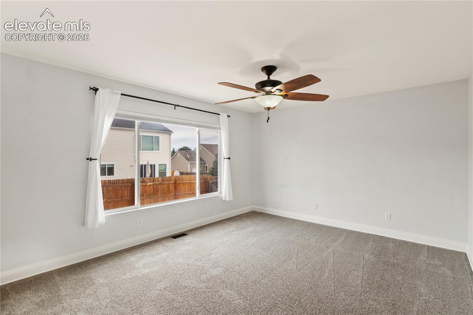 Neutral wall-to-wall carpeting, ceiling fan with integrated lighting, and large picture window