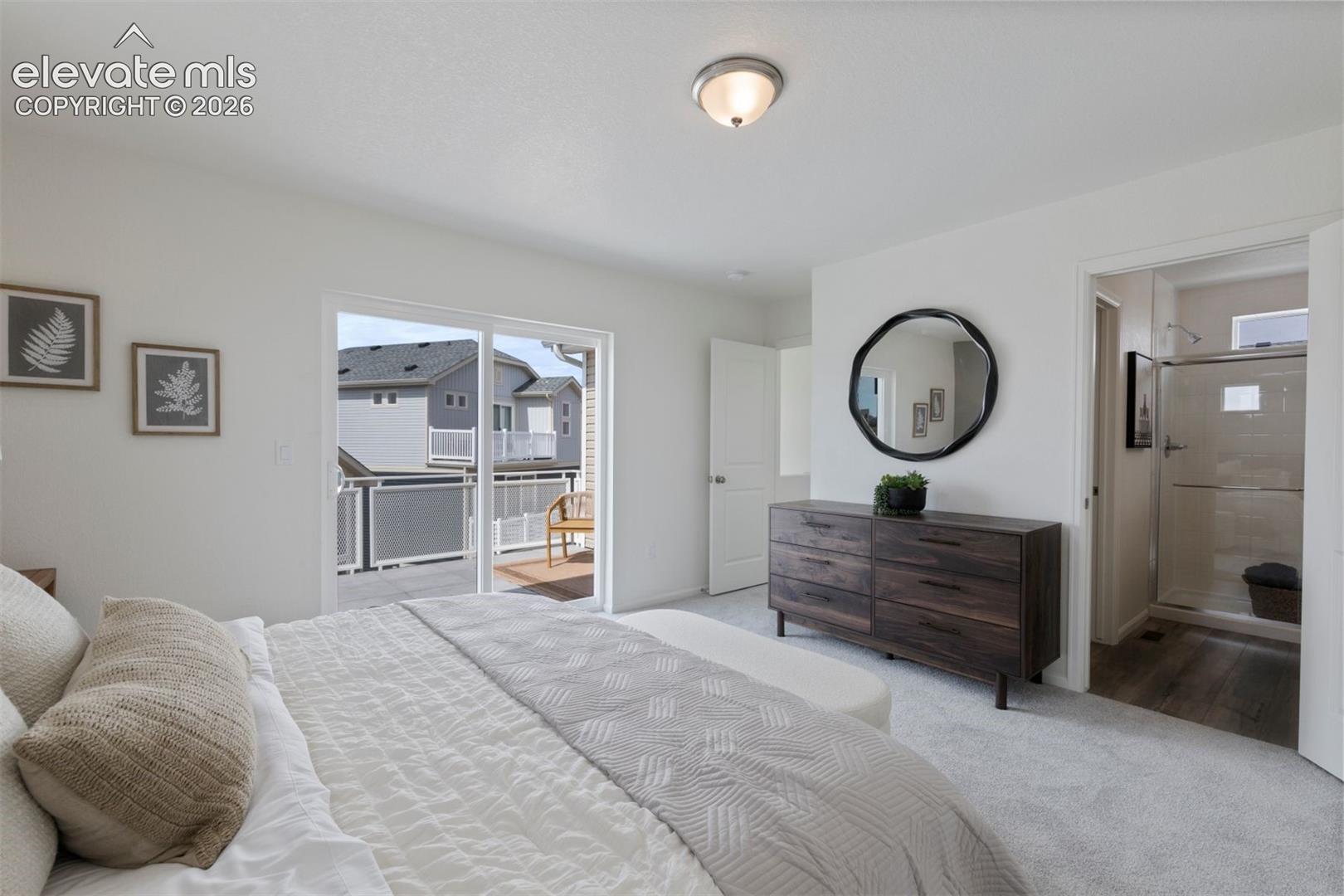 Sliding glass door leading to an outdoor balcony with wood-finish decking, light gray carpeting, and a full bathroom featuring a glass-enclosed shower
*photos of a model home*