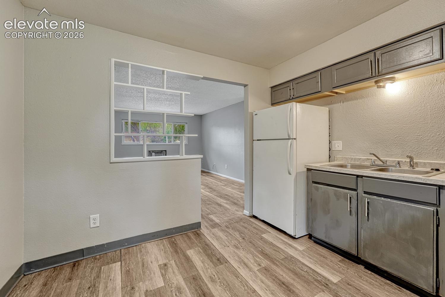 Kitchen featuring a double basin sink, gray cabinetry, a white refrigerator, and wood-finish flooring
