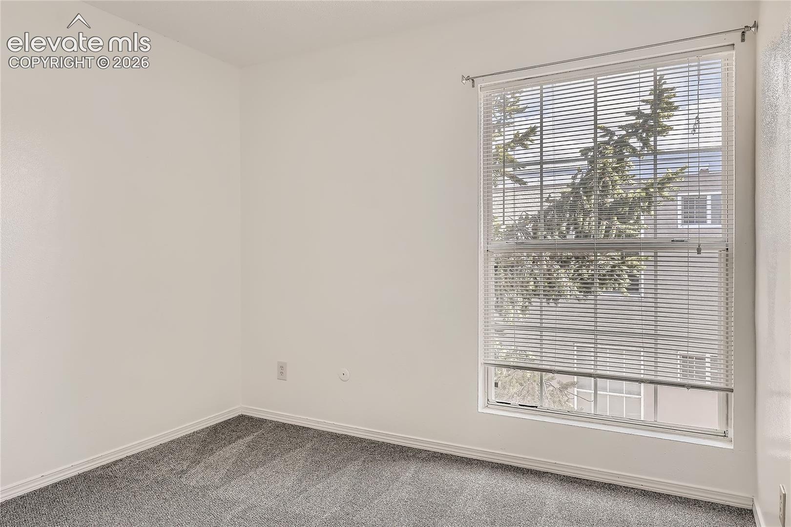Neutral-toned interior space featuring wall-to-wall carpeting and a single-hung window with horizontal blinds